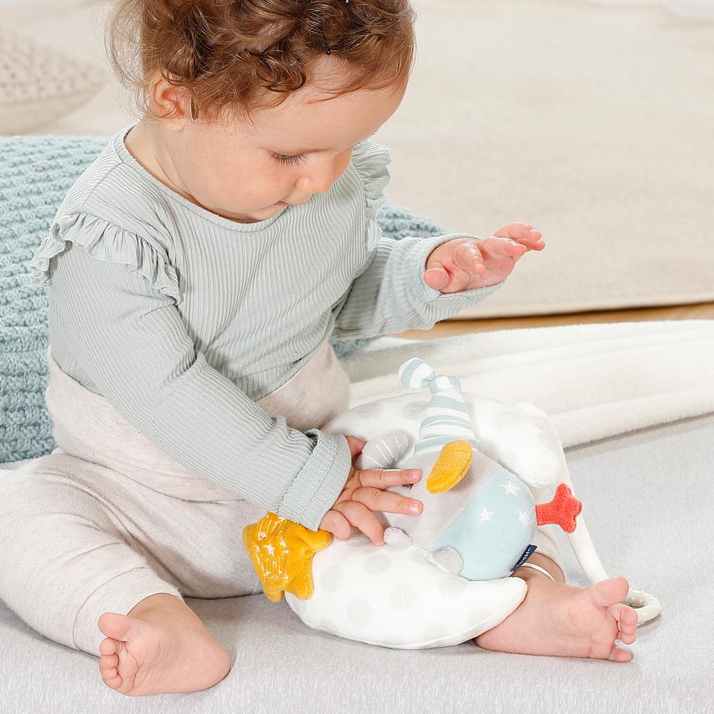 Ein Baby hält das Plüschelefantenspielzeug. Das Baby sitzt auf einem Bett.