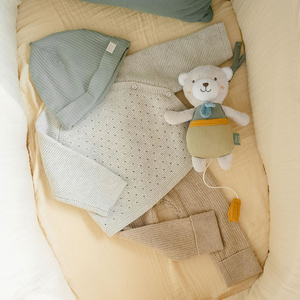 Articoli per bambini in una culla: cappello, coperta, pantaloni e un orsacchiotto.