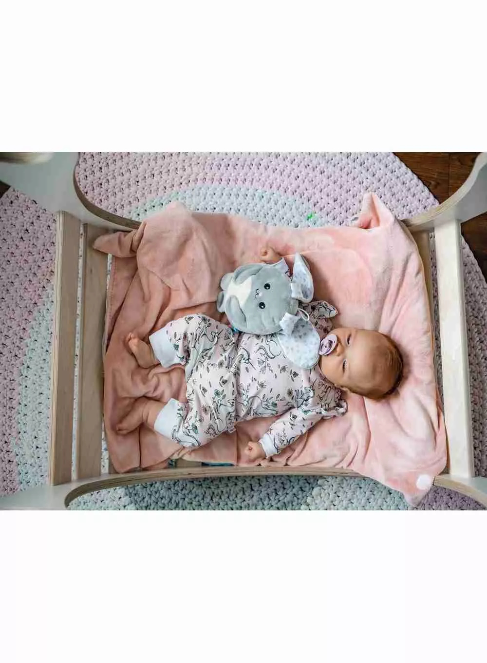 Bambino sdraiato in una culla con un elefante di peluche e un ciuccio.