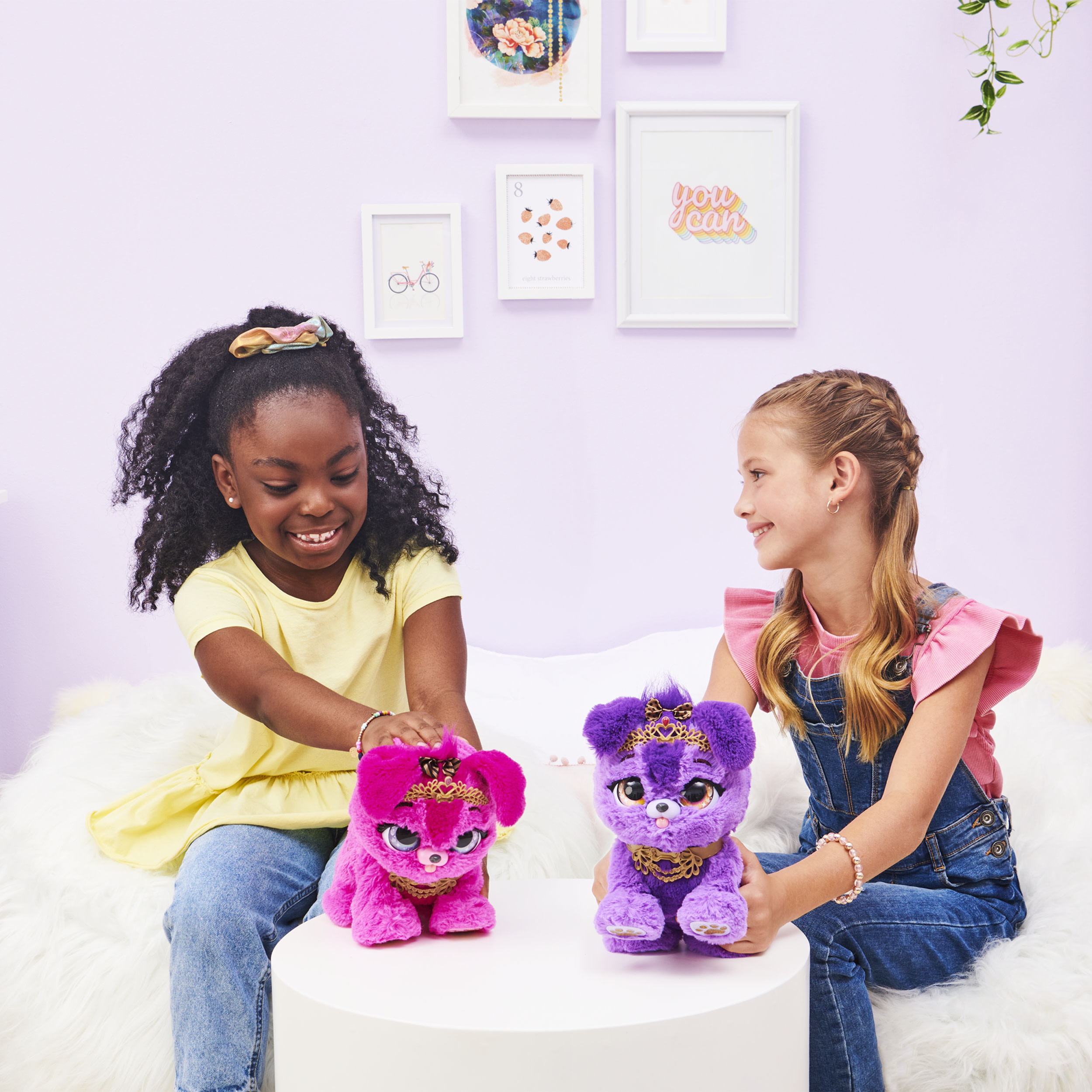Due ragazze giocano con cuccioli di peluche, uno rosa, l'altro viola, su un tavolo bianco.