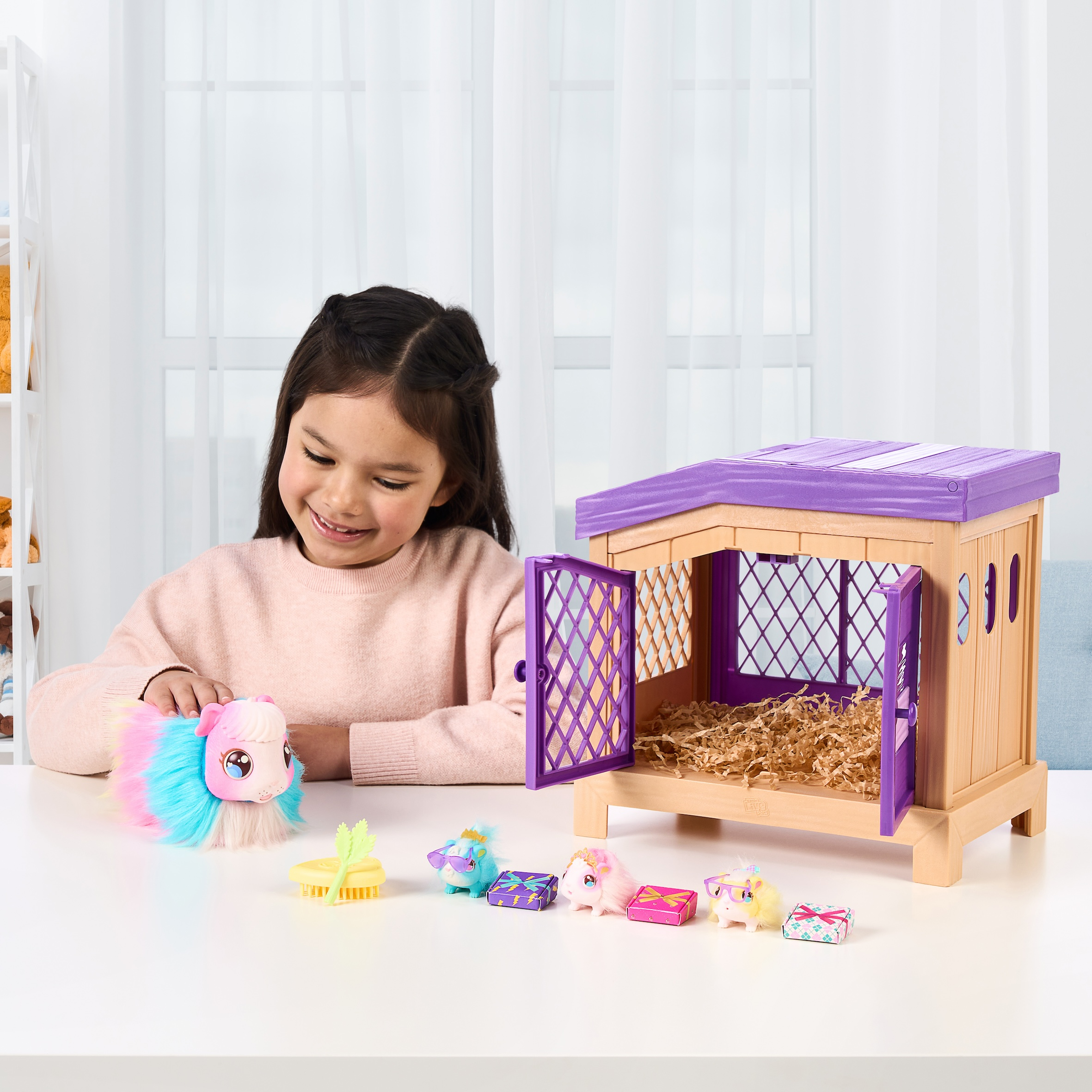 Bambina sorridente a un fienile giocattolo e pony, con tavolo bianco e sfondo finestra.