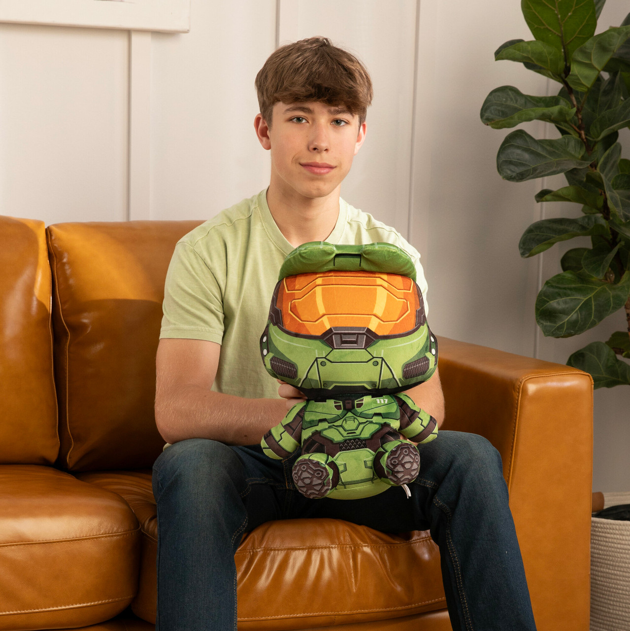 Młody mężczyzna siedzi i trzyma zielono-pomarańczową zabawkę. Zabawka to postać z kreskówki.