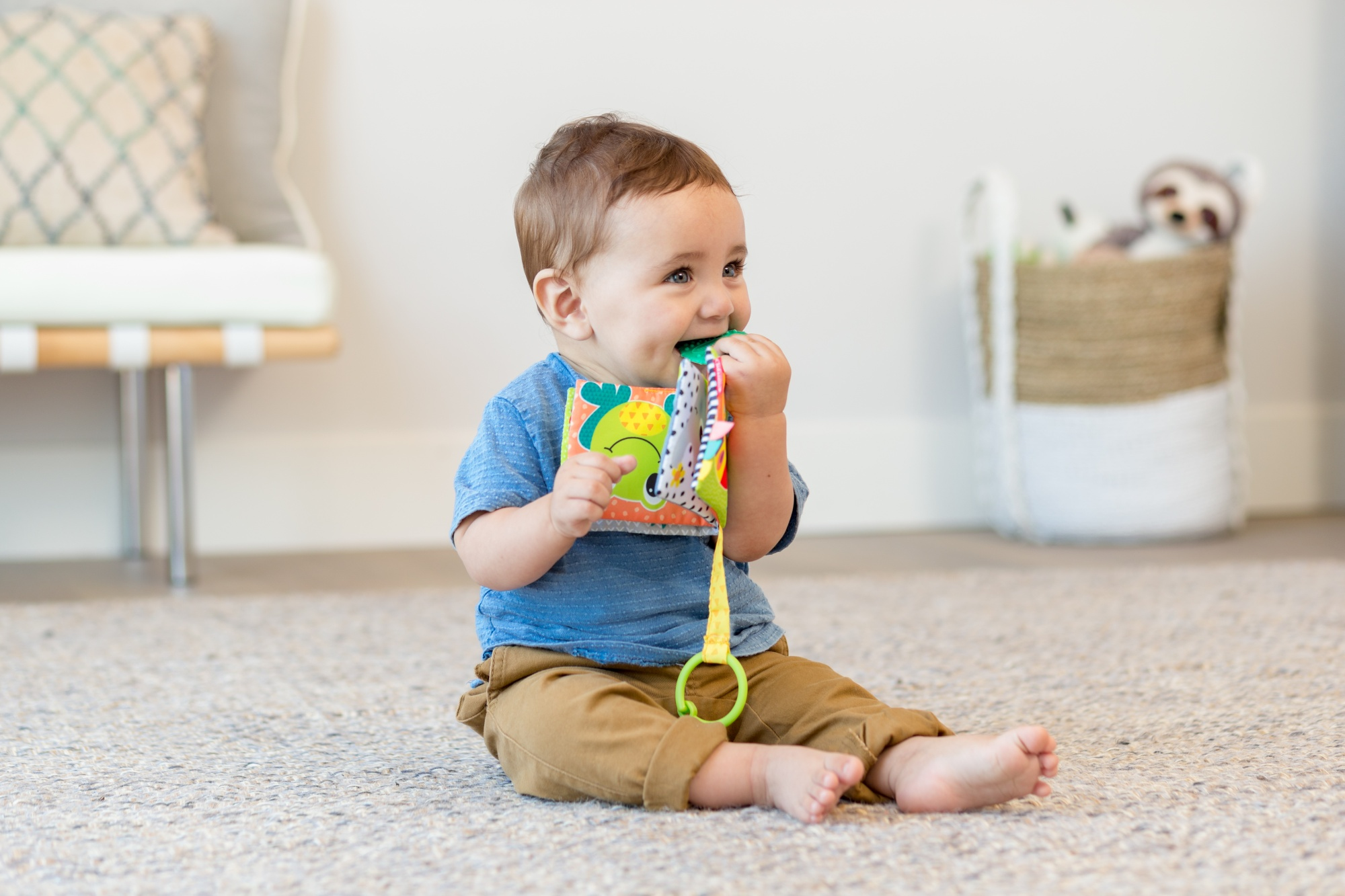 Bambino seduto su un tappeto, gioca con un libro colorato. Il bambino sorride.