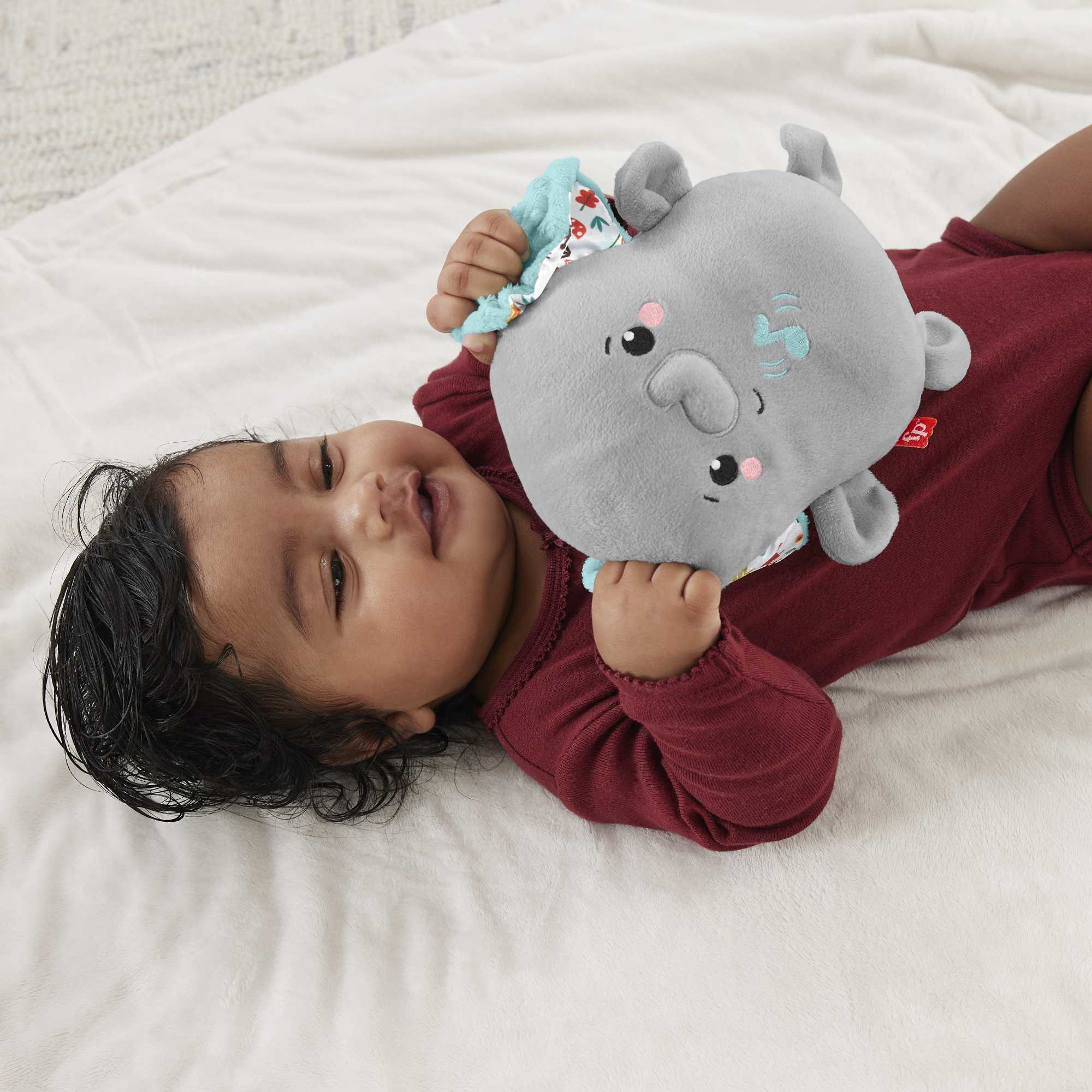 Ein Baby liegt auf einer weißen Decke und hält ein graues Elefanten-Plüschtier.