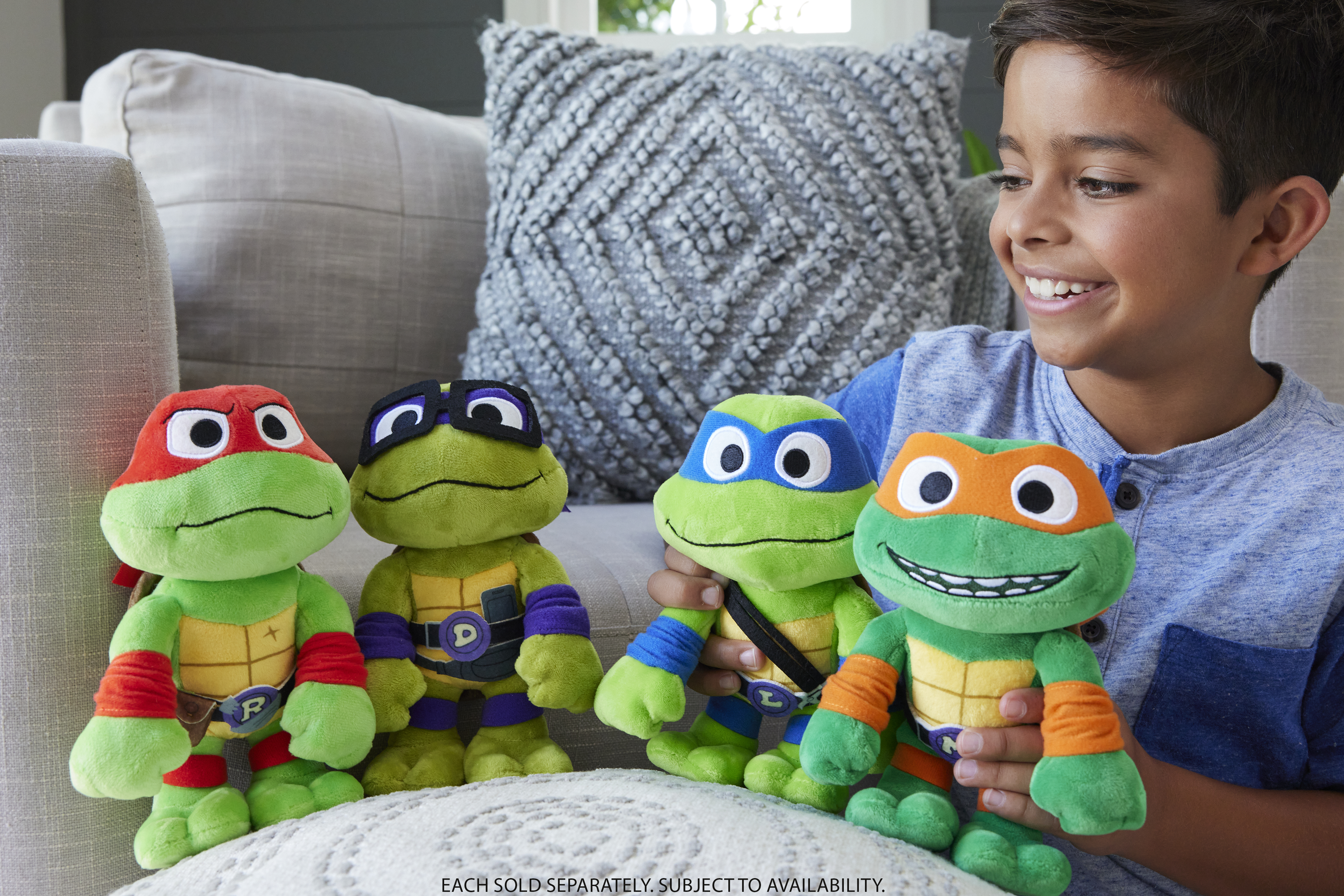 Ein Junge lächelt und hält vier Teenage Mutant Ninja Turtles-Plüschtiere. Sie sind grün mit verschiedenen Masken.
