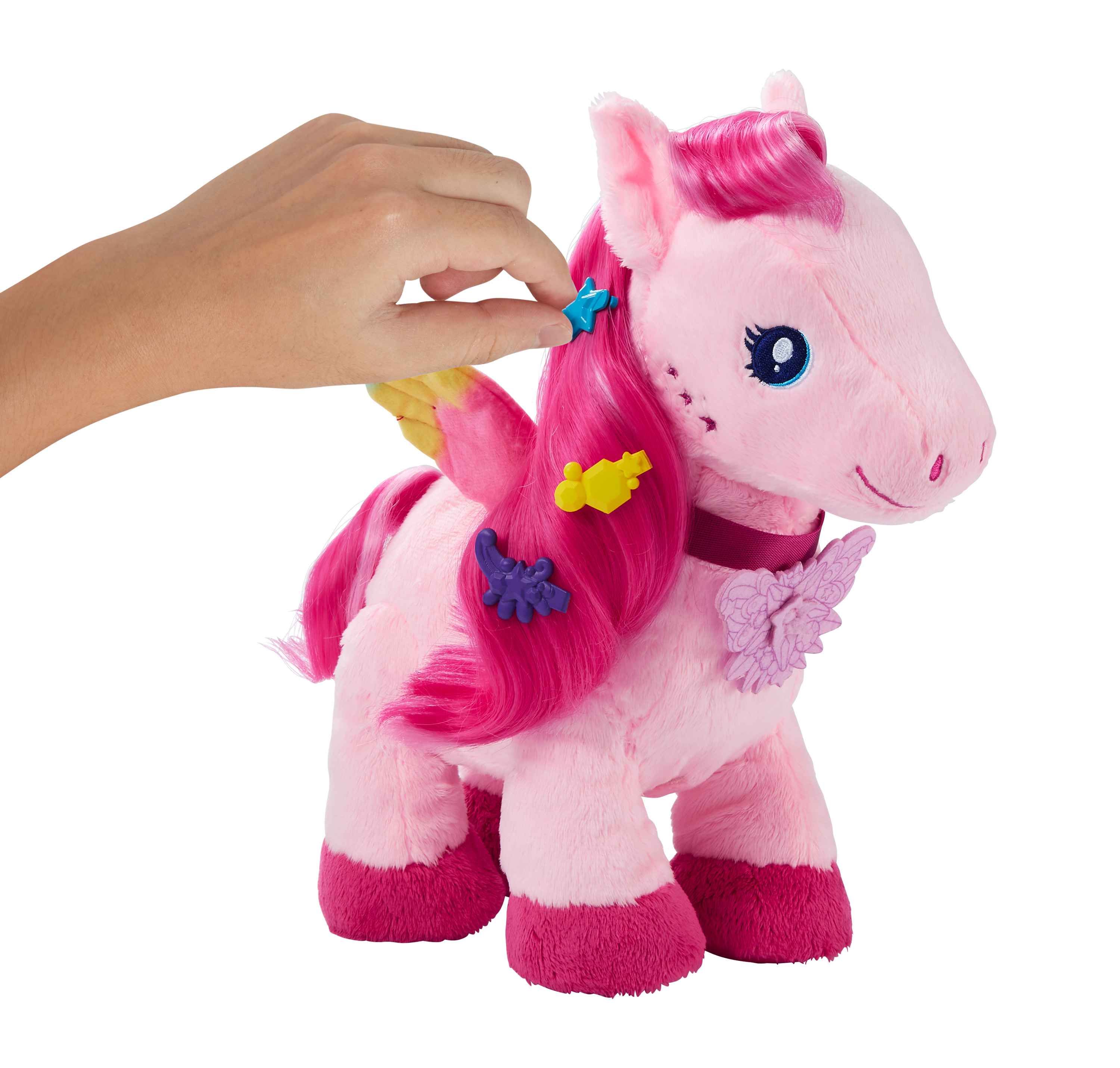 Eine Hand dekoriert ein rosa Plüscheinhorn mit Haarspangen. Das Einhorn hat Flügel und einen Schmetterling.