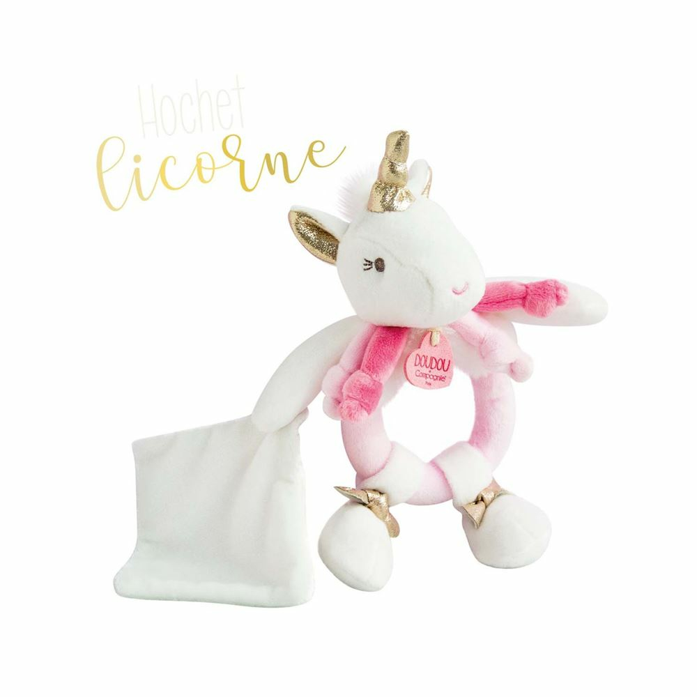 Biała pluszowa zabawka jednorożca z różową szarfą i złotymi akcentami. Biała poduszka po lewej.