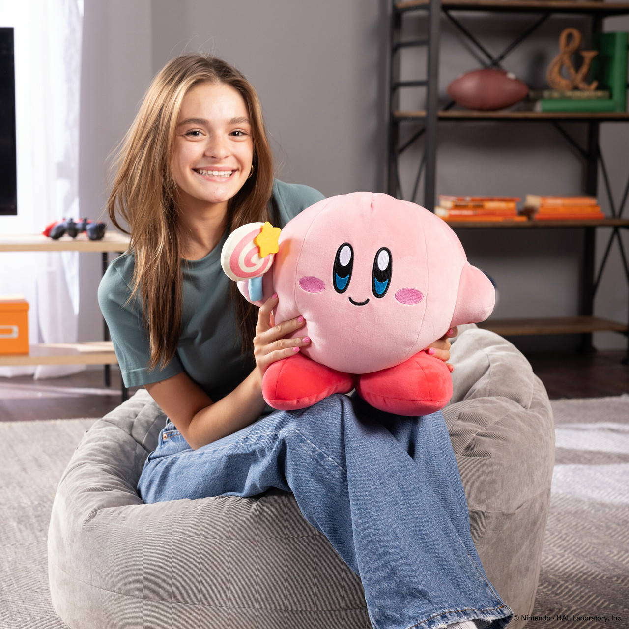 Una ragazza che tiene un peluche rosa di Kirby con un lecca-lecca, seduta.