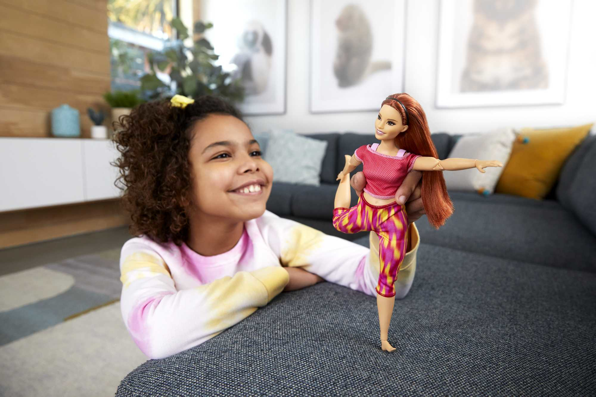 Ein lächelndes Mädchen, das eine Barbie-Puppe in Yoga-Pose hält, mit unscharfem Hintergrund.