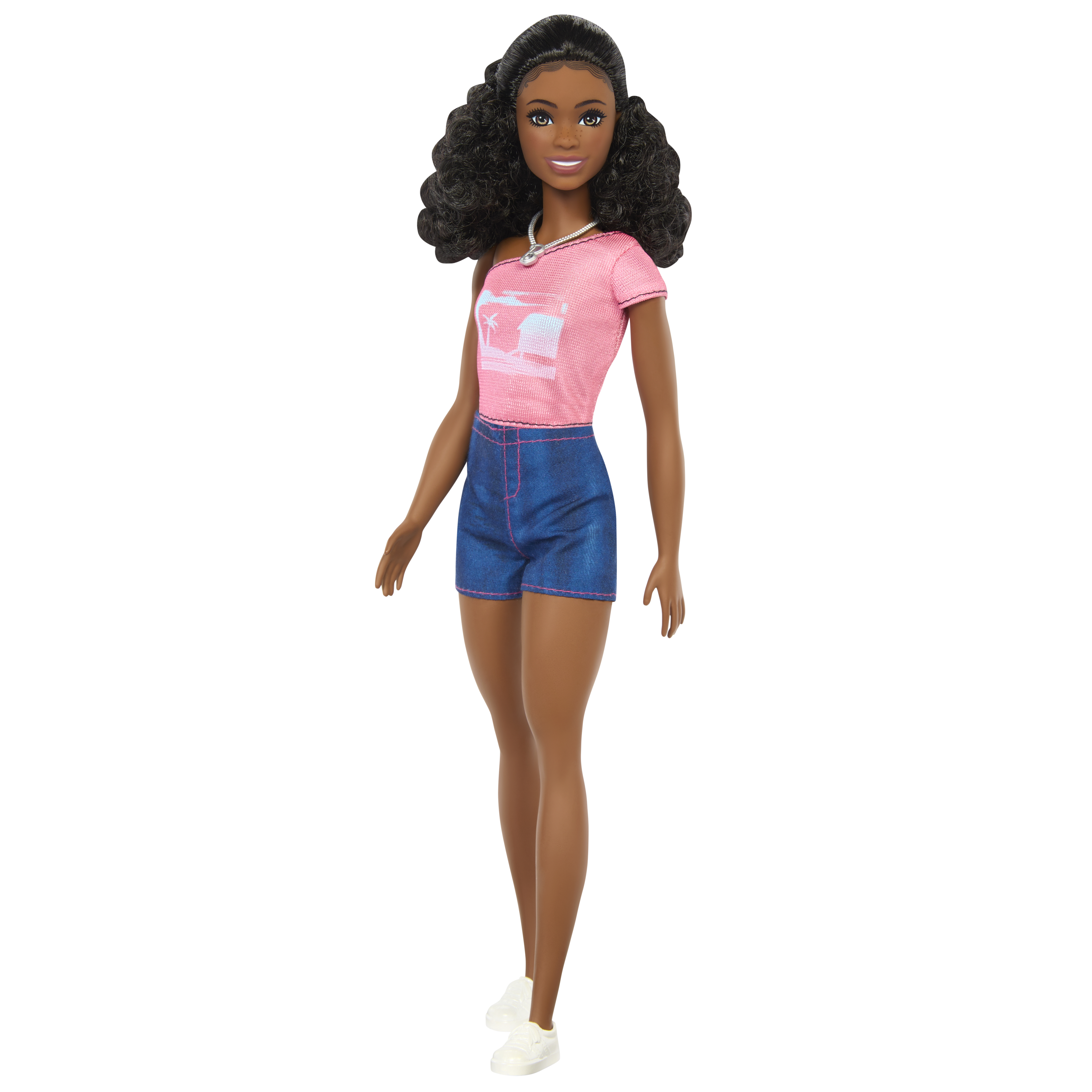 Eine Puppe mit dunkler Haut, lockigem schwarzem Haar und einem rosa Hemd. Sie trägt Jeansshorts und weiße Turnschuhe.