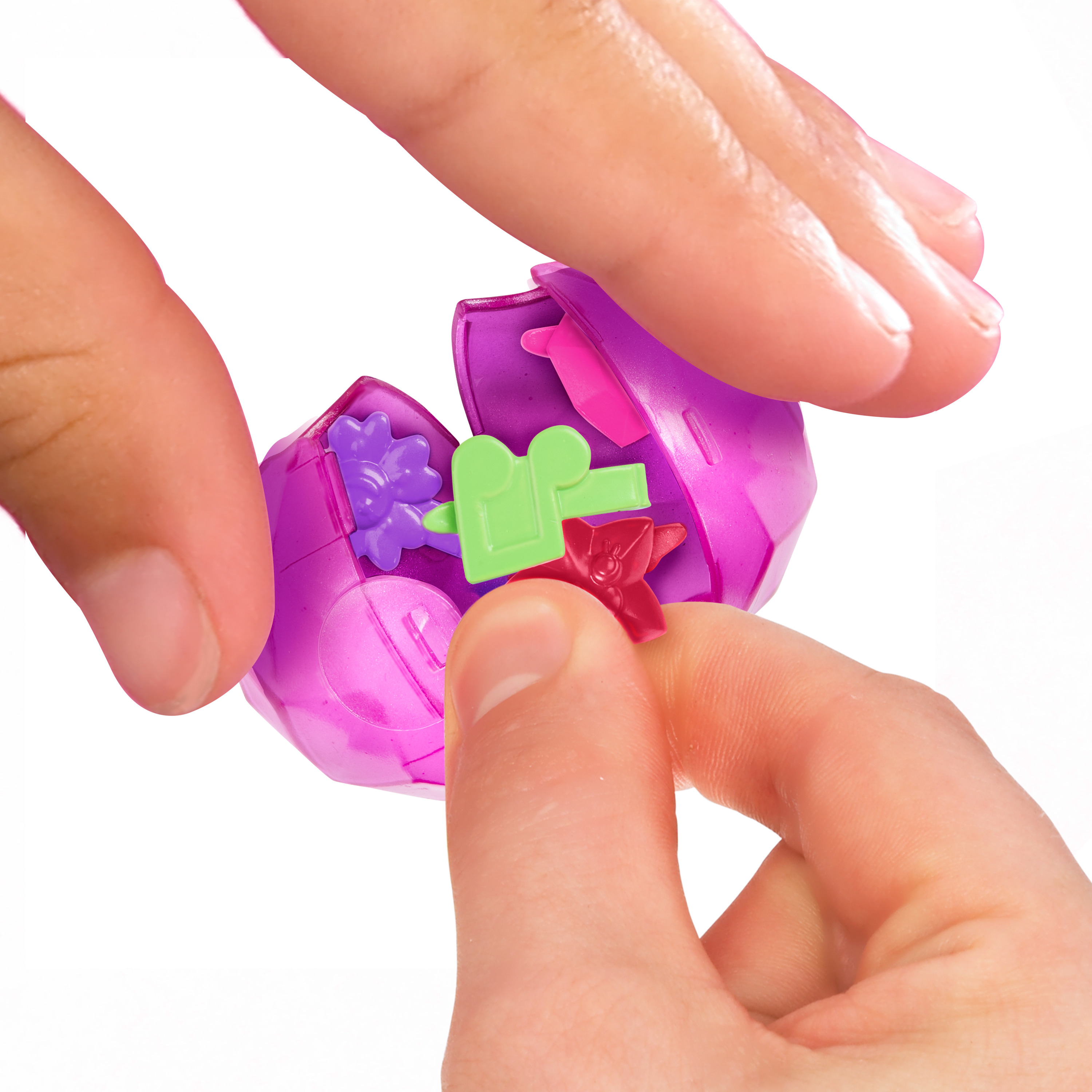 Mani che aprono un uovo di plastica viola con piccoli pezzi di giocattoli colorati all'interno. Sfondo bianco.