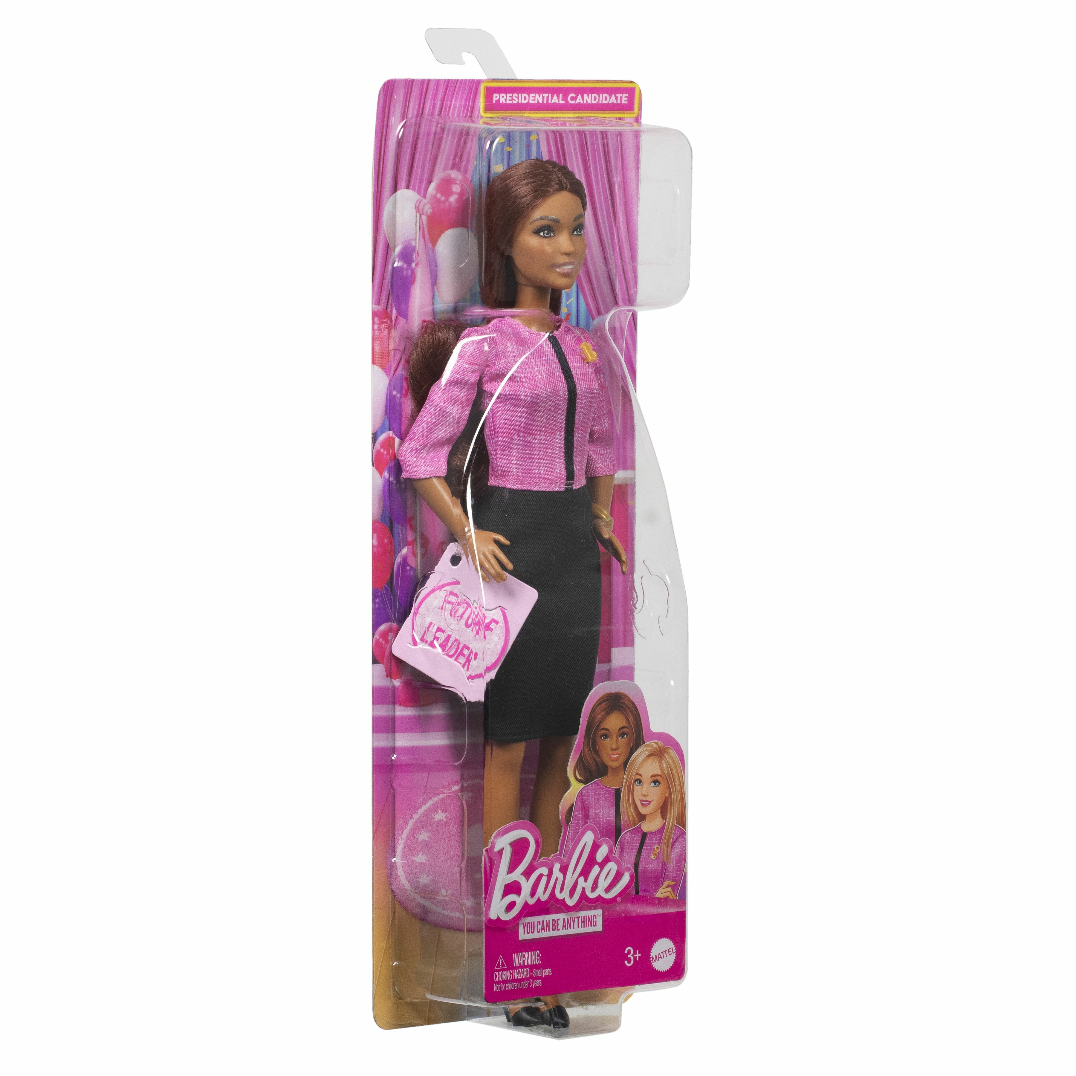 Eine Barbie-Puppe in einer Schachtel, die als Präsidentschaftskandidatin gekleidet ist. Sie trägt eine rosa Jacke und einen schwarzen Rock.