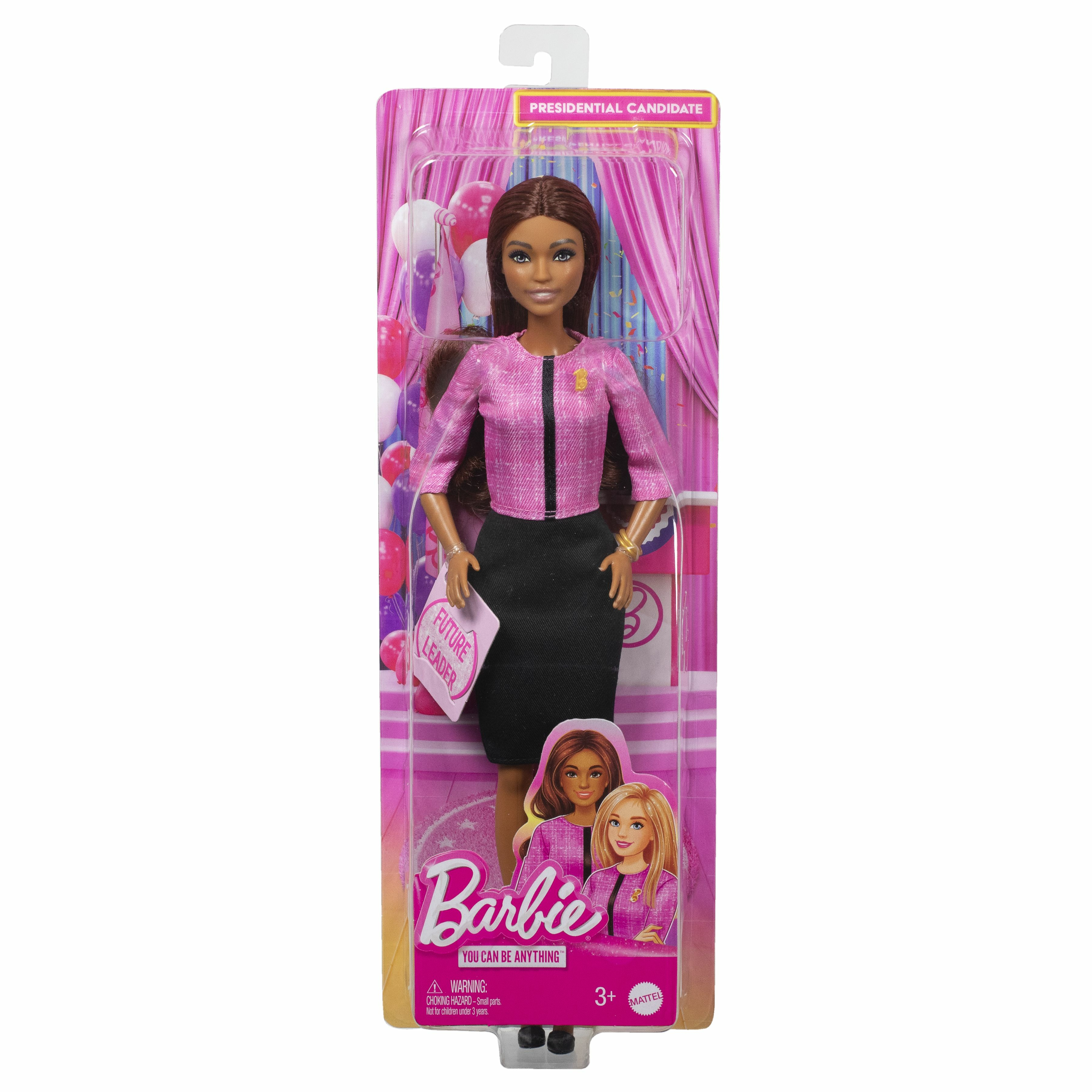 Eine Barbie-Puppe in einer rosa Jacke und einem schwarzen Rock ist in einer Verpackung. Sie hat ein Schild mit der Aufschrift 'Future Leader'.