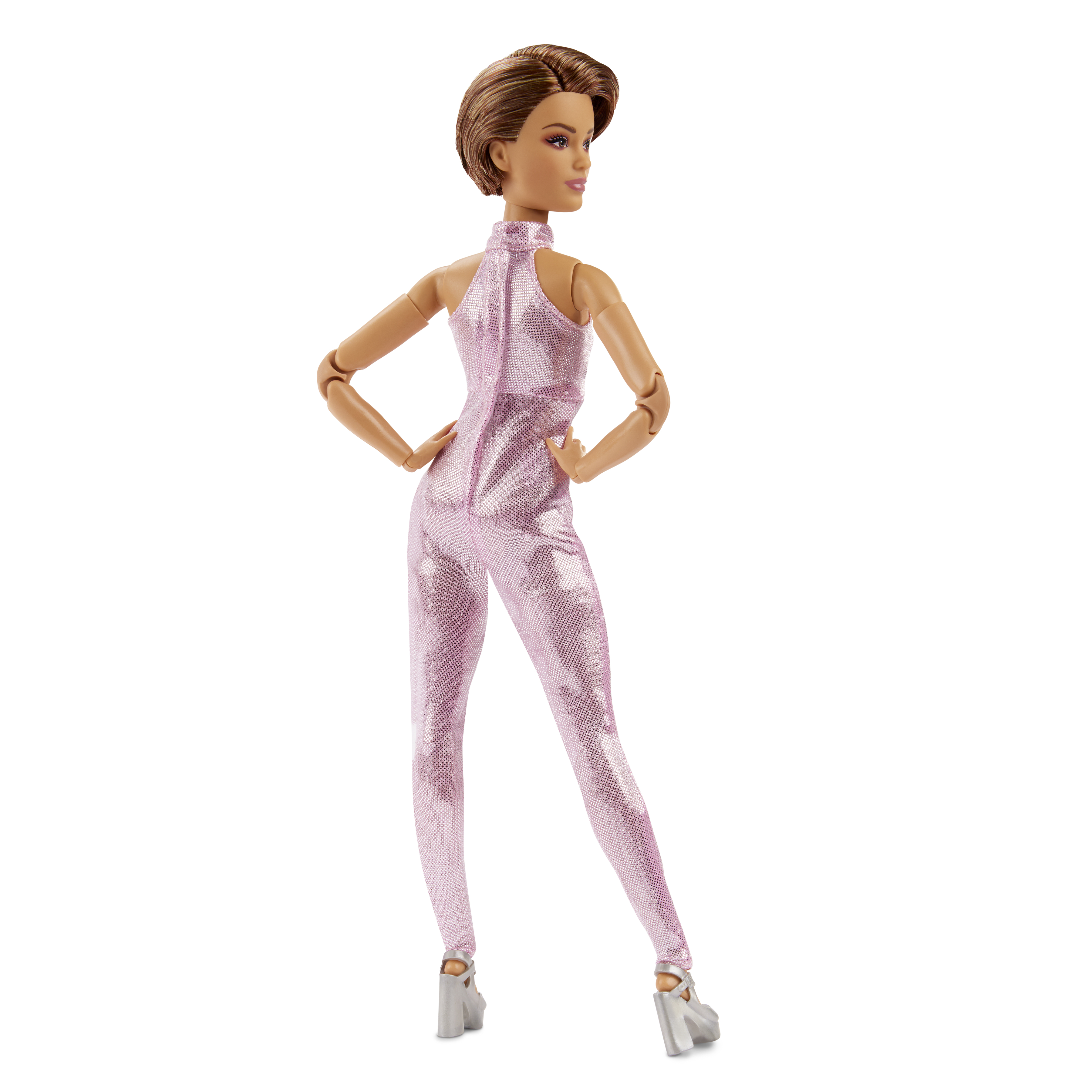Eine Barbie-Puppe in einem rosa, glitzernden Overall. Sie steht mit den Händen in den Hüften.