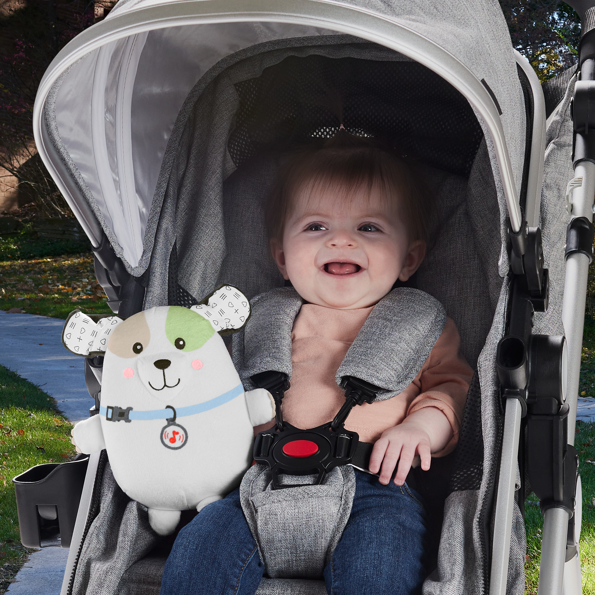Ein Baby in einem Kinderwagen mit einem Plüschhund. Das Baby lächelt und trägt einen Gurt.