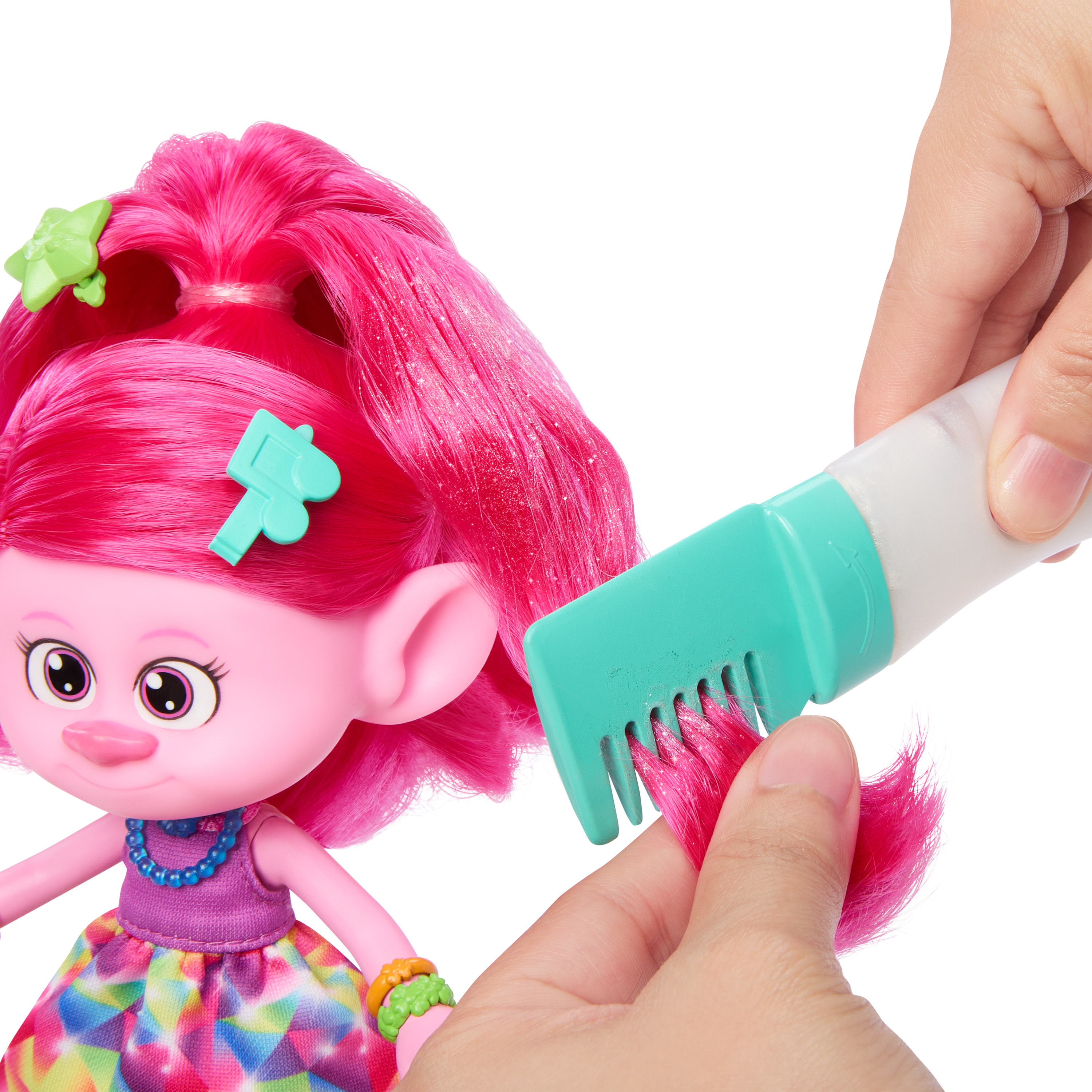 Eine Person kämmt mit einem Kamm die rosa Haare einer Troll-Puppe. Grünes Haaraccessoire in Blumenform.