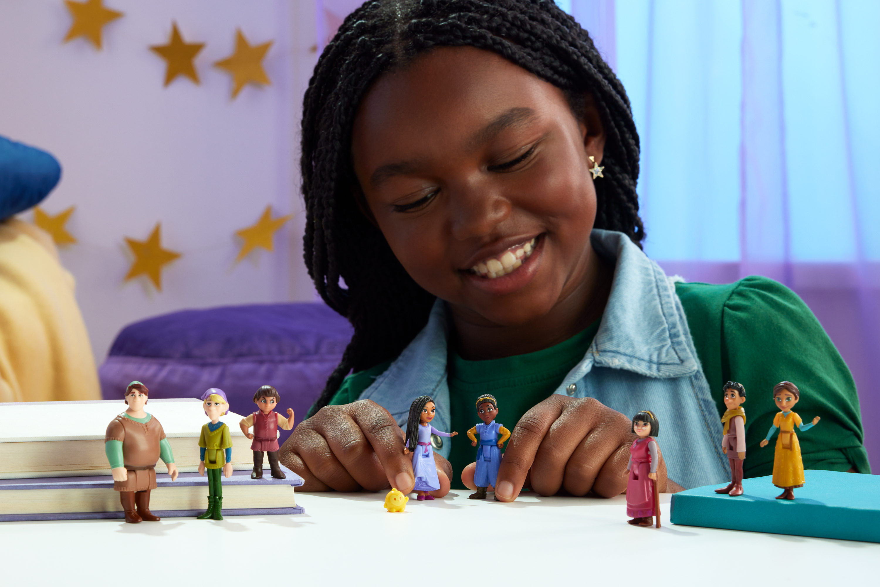 Dziewczynka uśmiecha się do lalek. Lalki na stole. Żółte gwiazdy w tle.