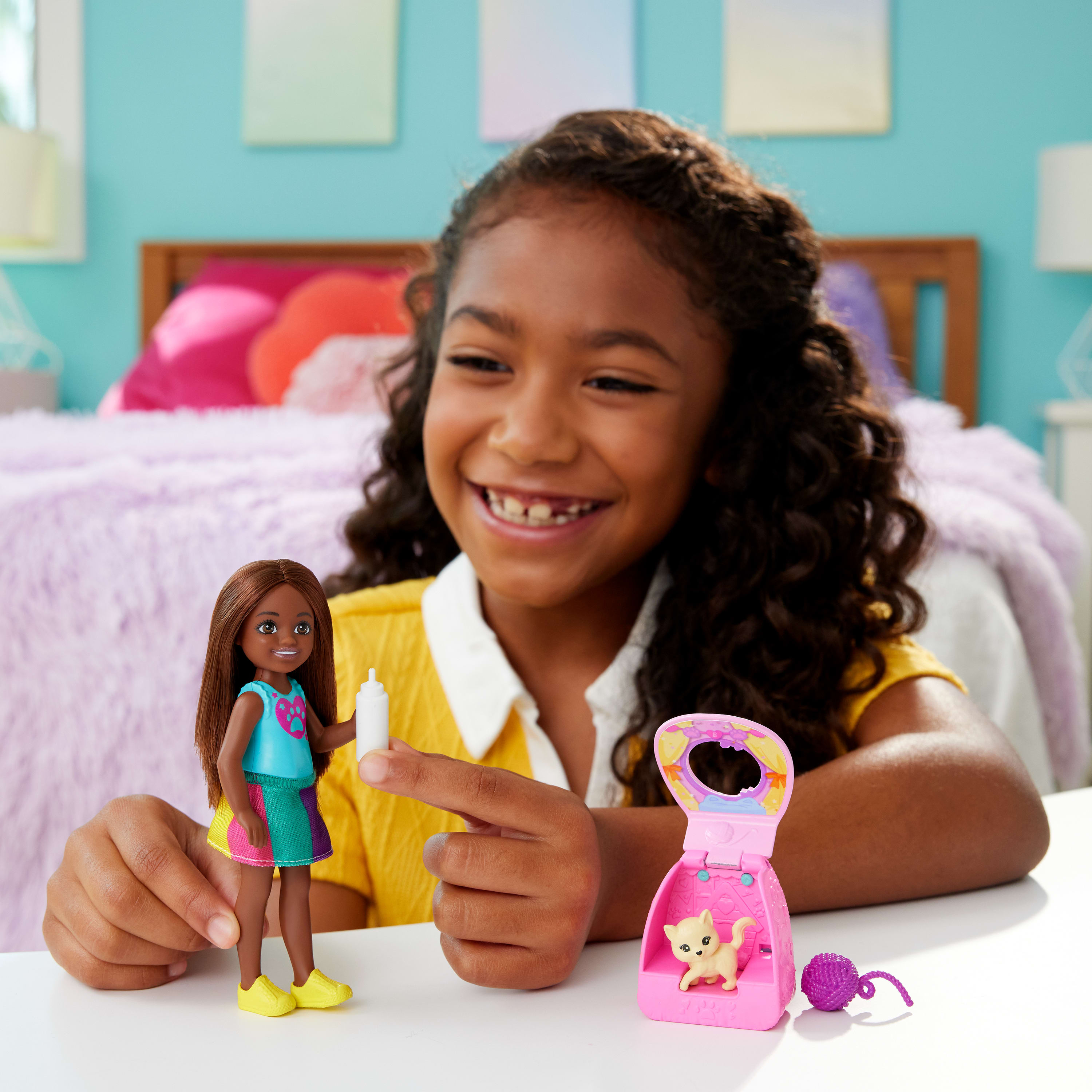 Dziewczynka bawiąca się lalką Chelsea i akcesoriami. Lalka trzyma butelkę, jest domek dla kota.