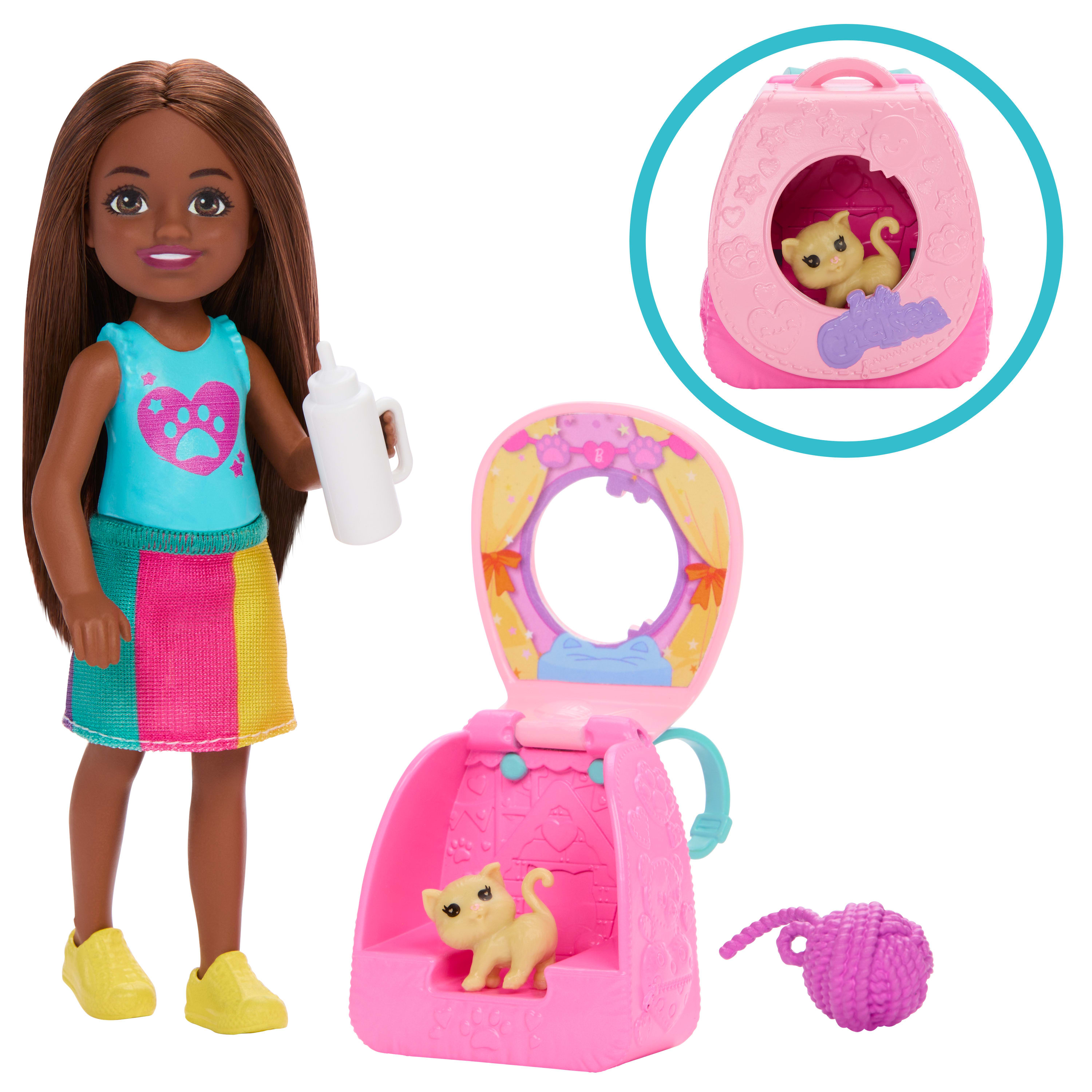 Lalka Chelsea trzymająca butelkę, obok domku dla lalek z kotkiem i kulą włóczki.