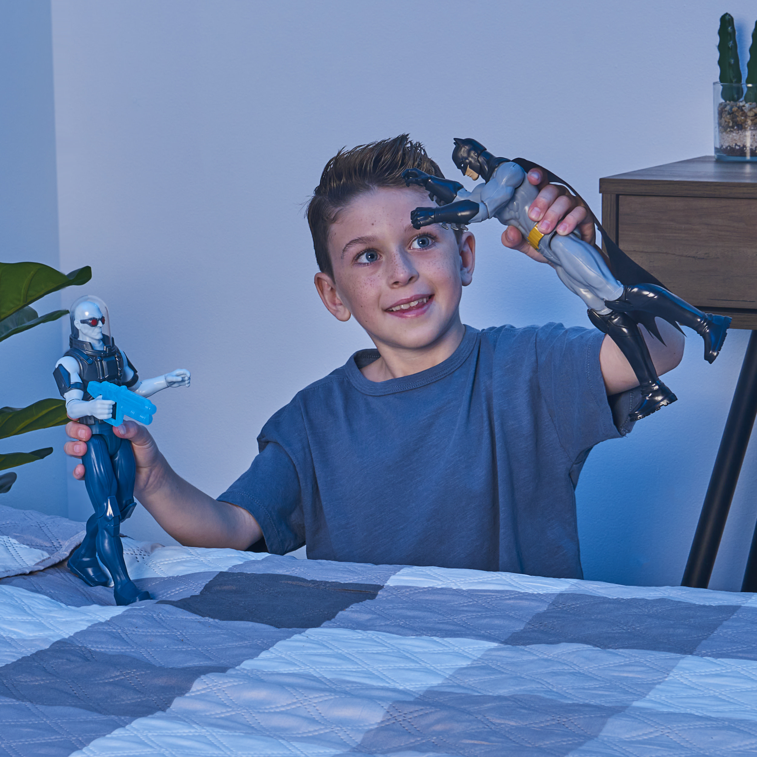 Chłopiec bawiący się figurkami Batmana i Mr. Freeze w pokoju z rośliną i łóżkiem.