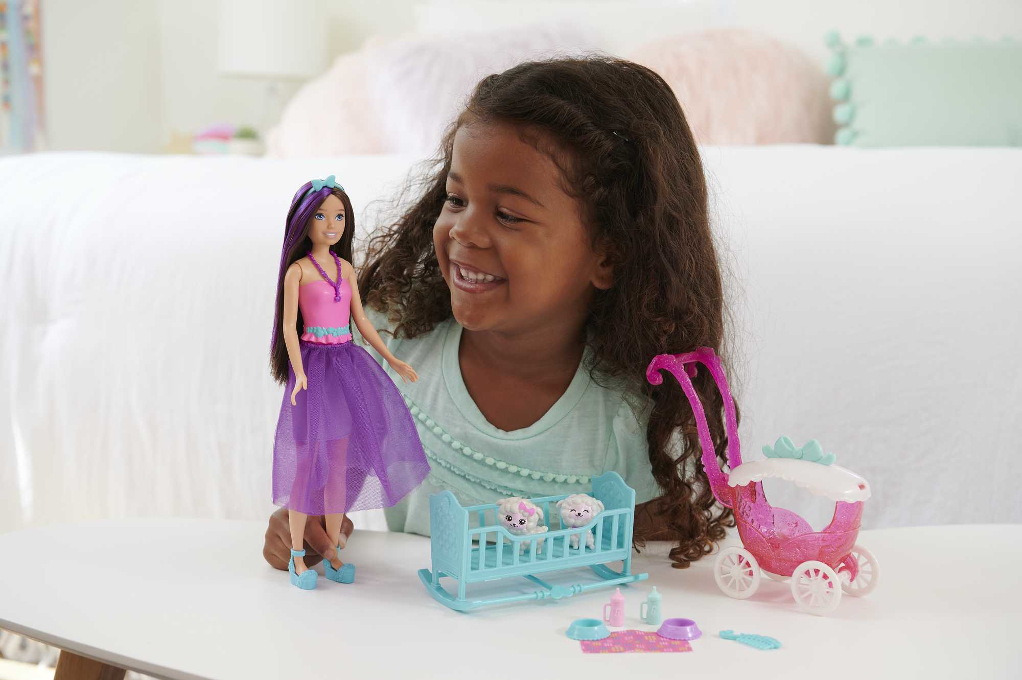 Młoda dziewczyna uśmiecha się trzymając lalkę. Obecny jest wózek dziecięcy i inne zabawki.