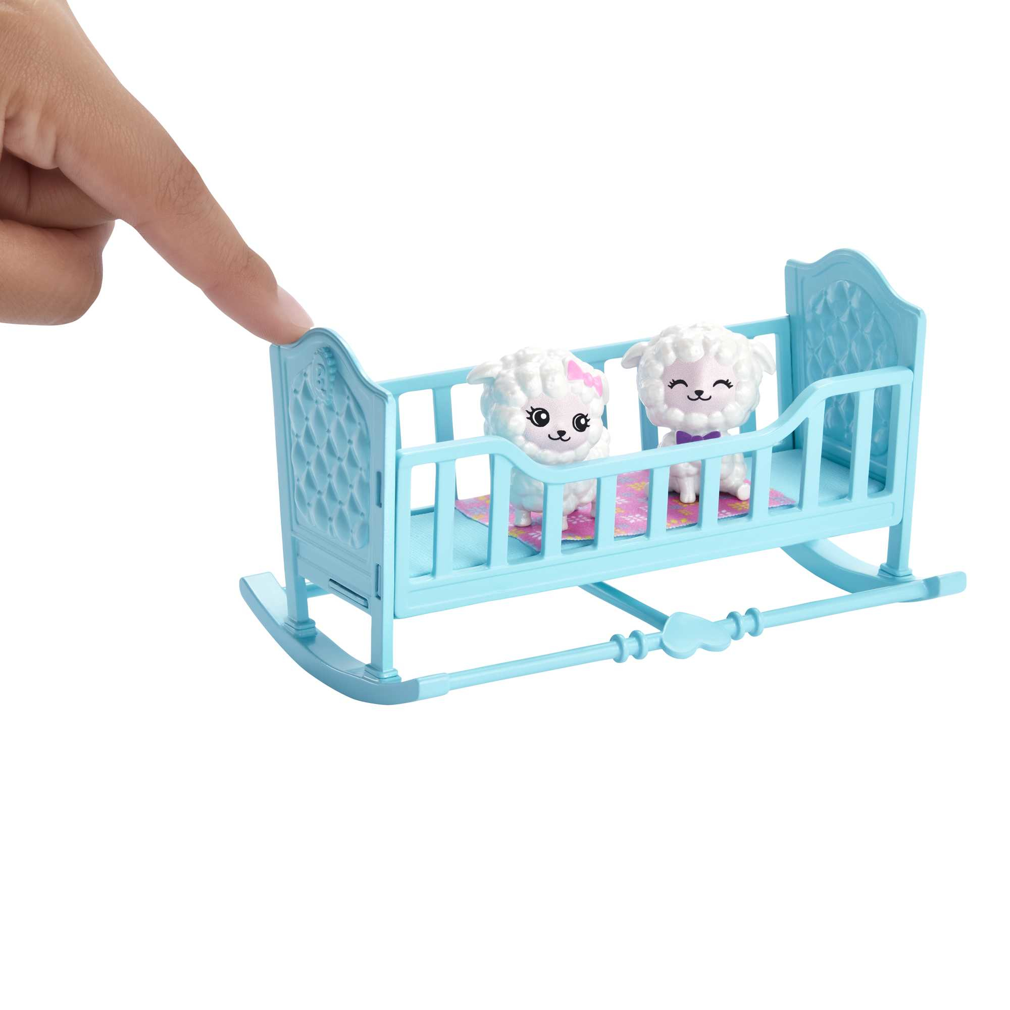 Dłoń wskazuje na dwie zabawki owiec w niebieskim łóżeczku.