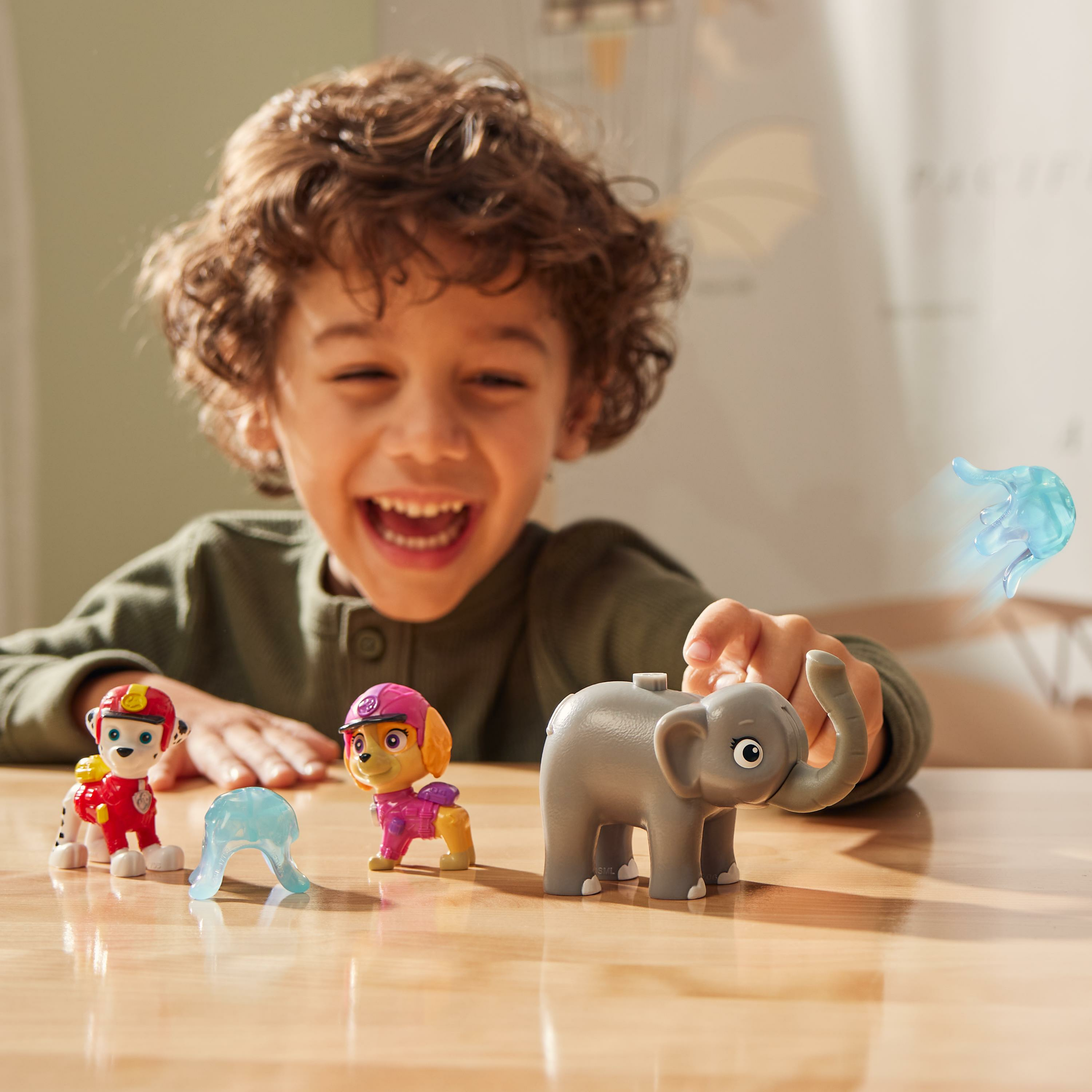 Il ragazzo gioca con i giocattoli di Paw Patrol, tra cui un elefante grigio giocattolo e due figure di cani. Il ragazzo sta sorridendo.