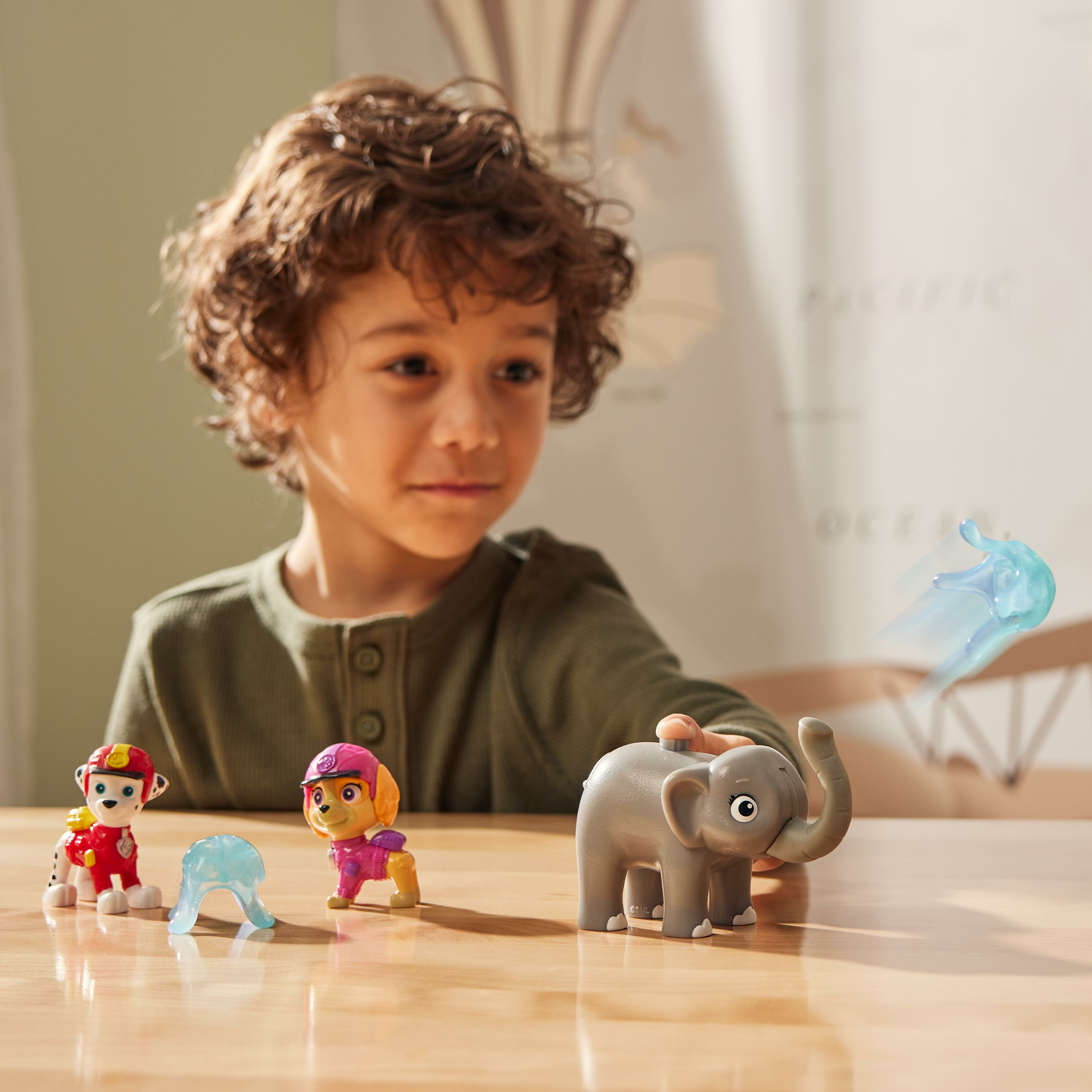 Un ragazzo con giocattoli, tra cui personaggi di Paw Patrol e un elefante, su un tavolo.