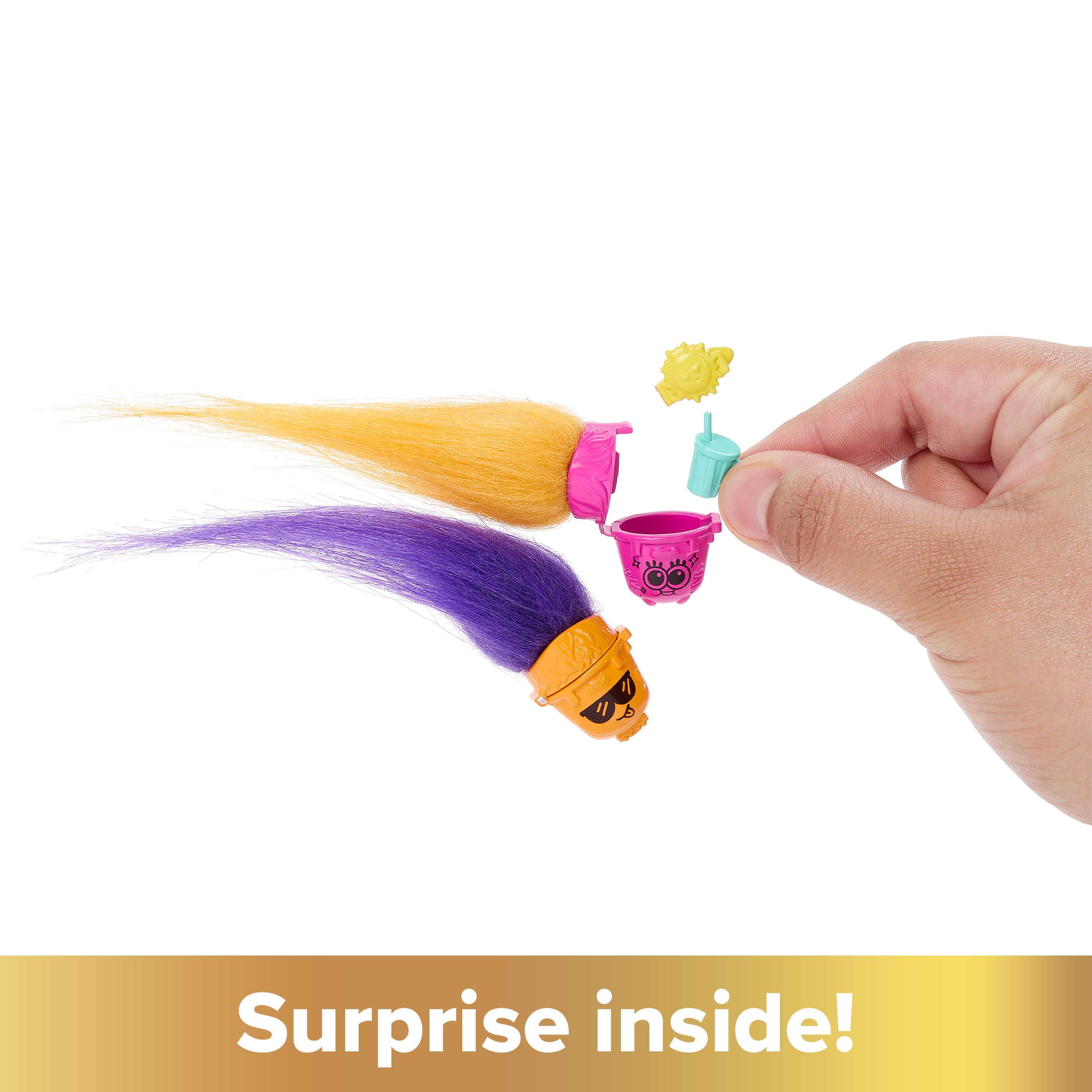 Dłoń trzymająca parę zabawek, akcesoriów do włosów. U dołu widnieje napis 'Niespodzianka w środku!'.