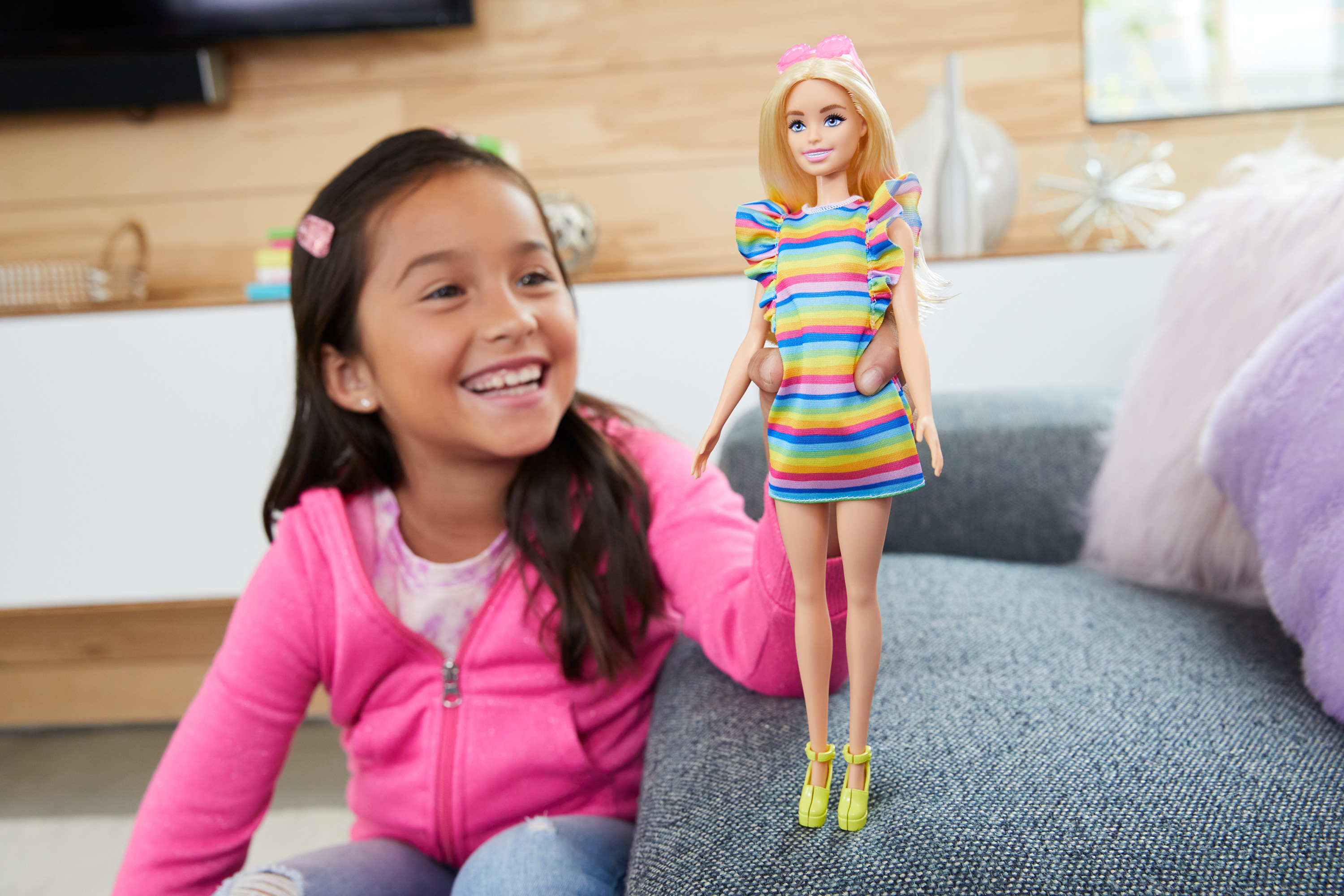 Ein Mädchen hält eine Barbie-Puppe. Die Puppe hat ein buntes Kleid und blondes Haar.