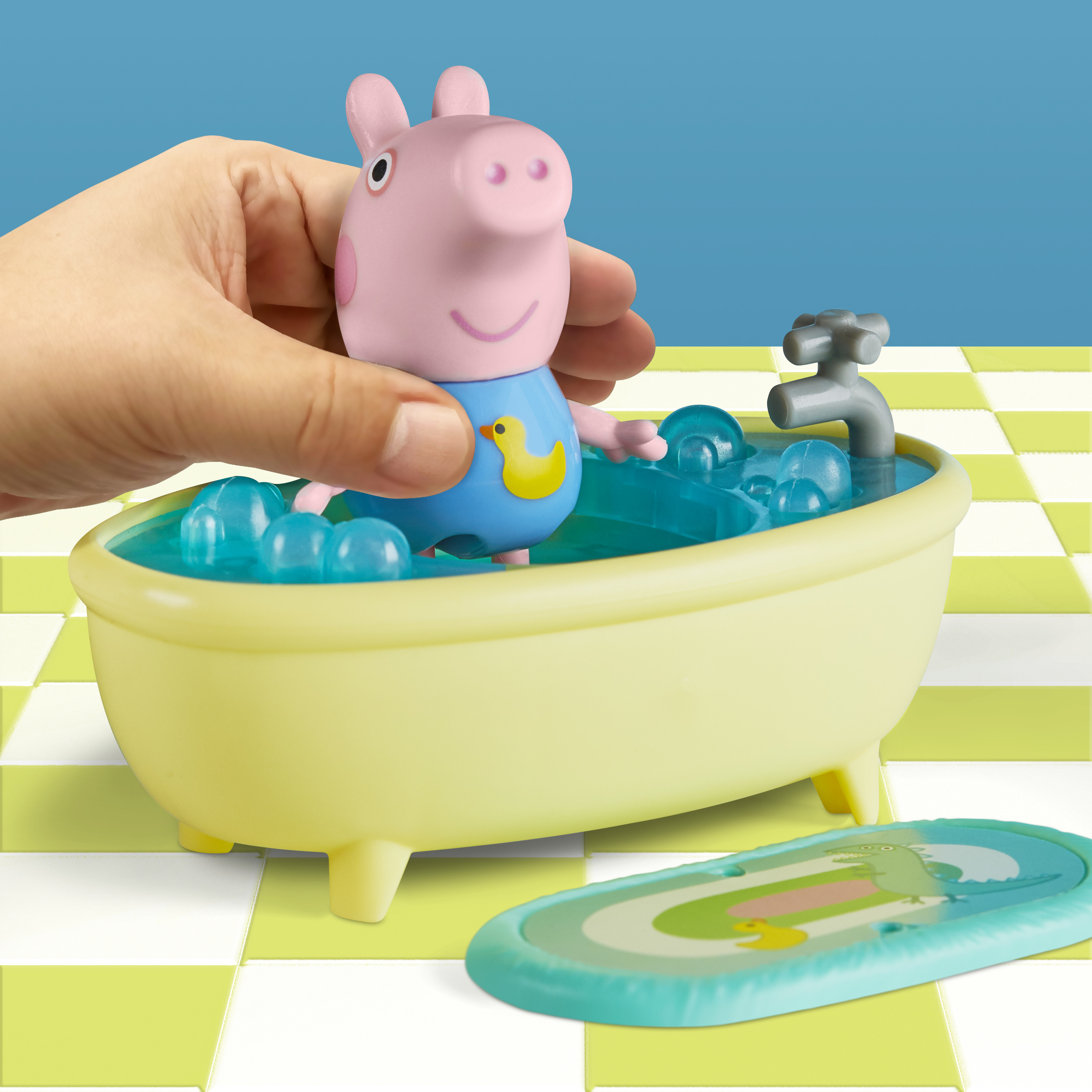 Peppa Pig in una vasca da bagno gialla con bolle. Una mano tiene la figura su uno sfondo a scacchi blu e verde.
