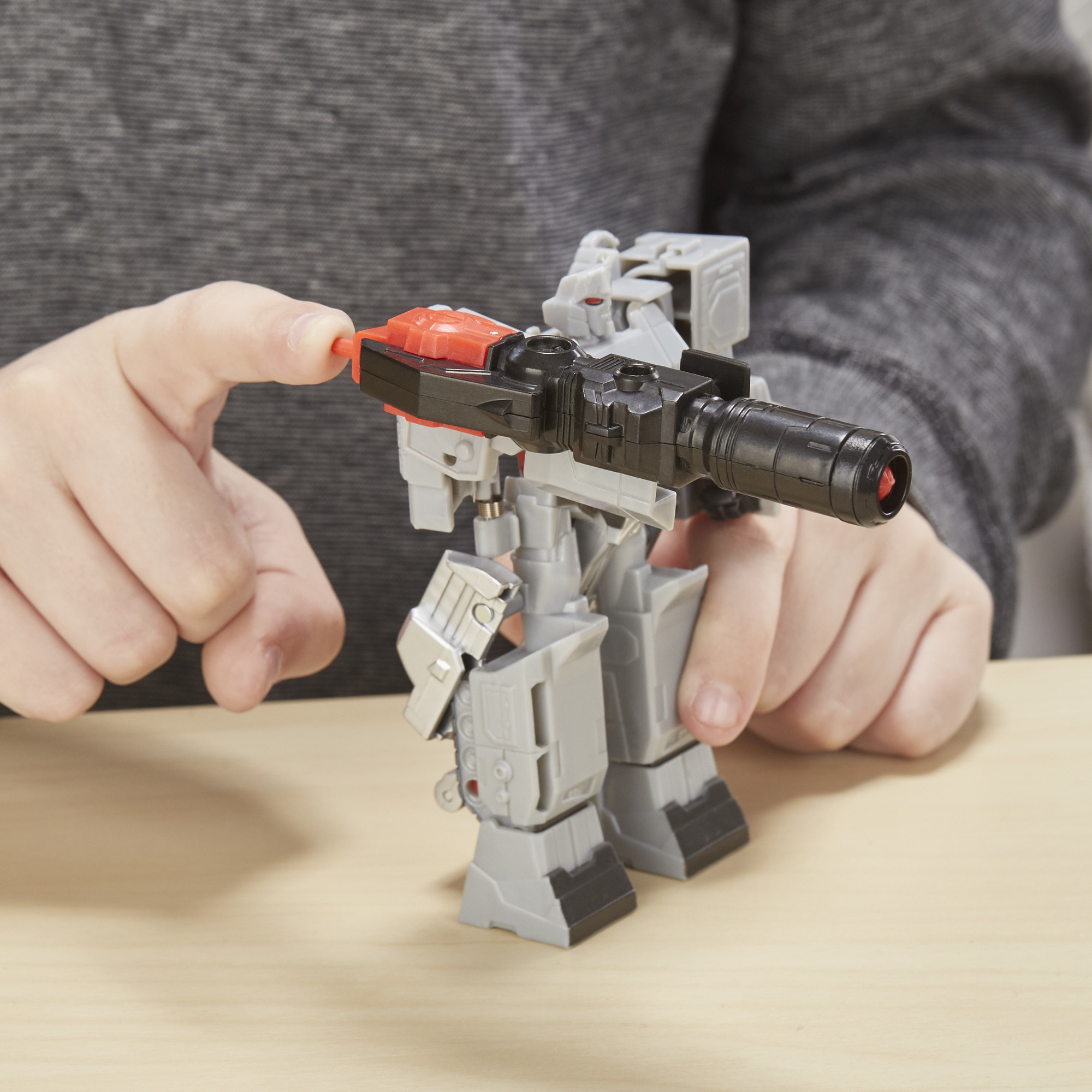 Die Hände einer Person, die ein graues Megatron-Transformer-Spielzeug anpassen.
