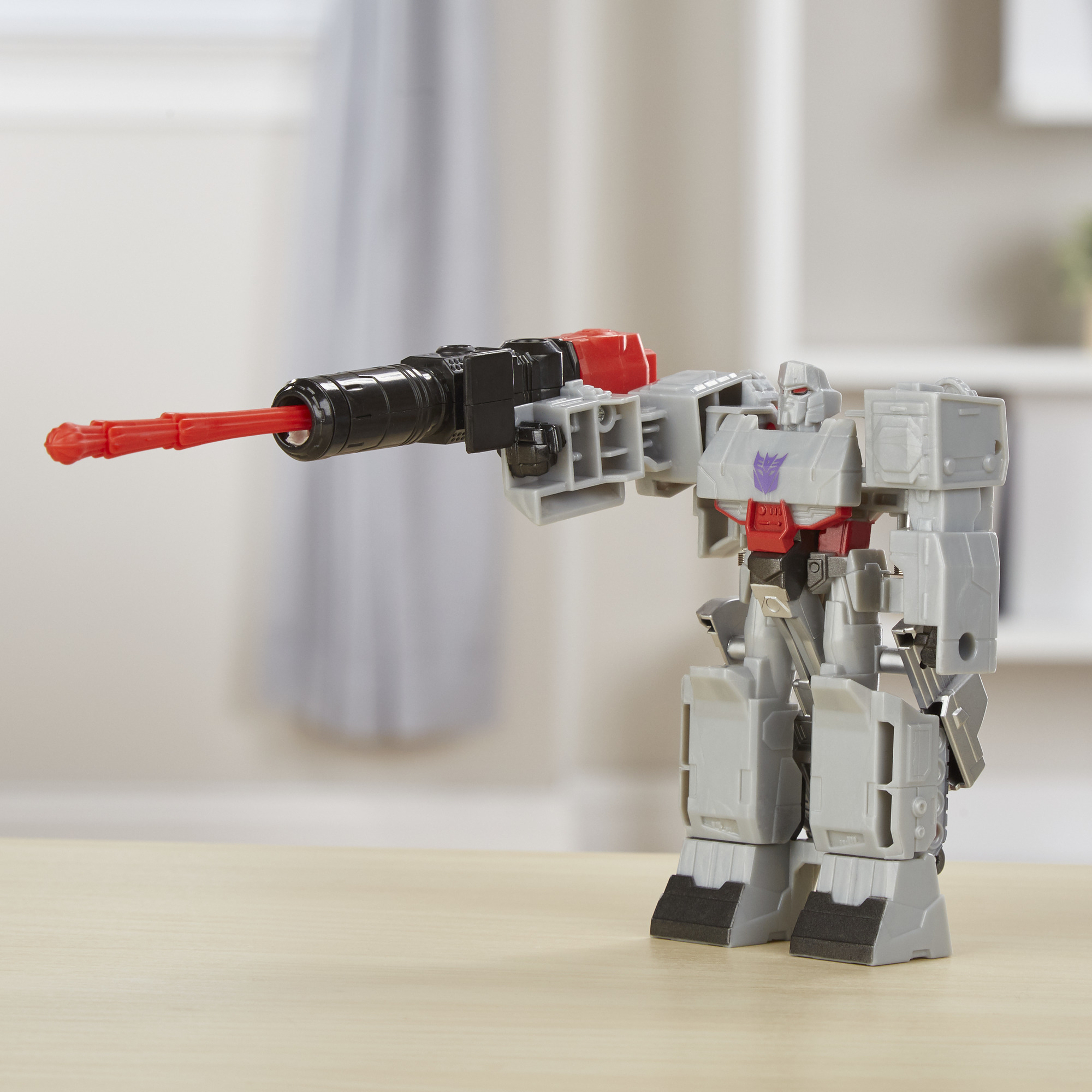 Graues Megatron Transformer Spielzeug, das eine große Waffe hält. Vor einem verschwommenen Hintergrund mit Holzoberfläche.
