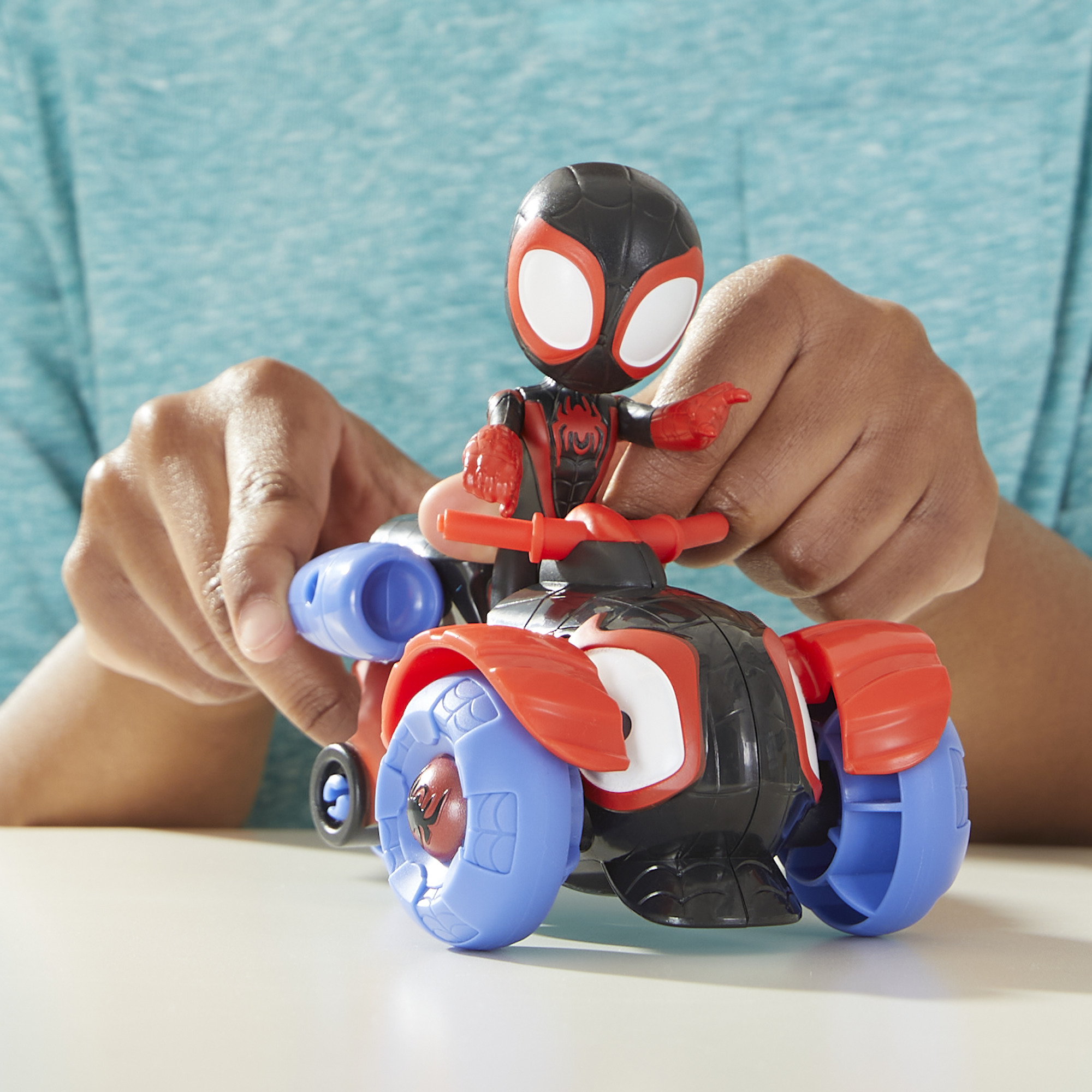 Mani di una persona che tiene un giocattolo di Miles Morales Spider-Man su una moto rossa e nera.