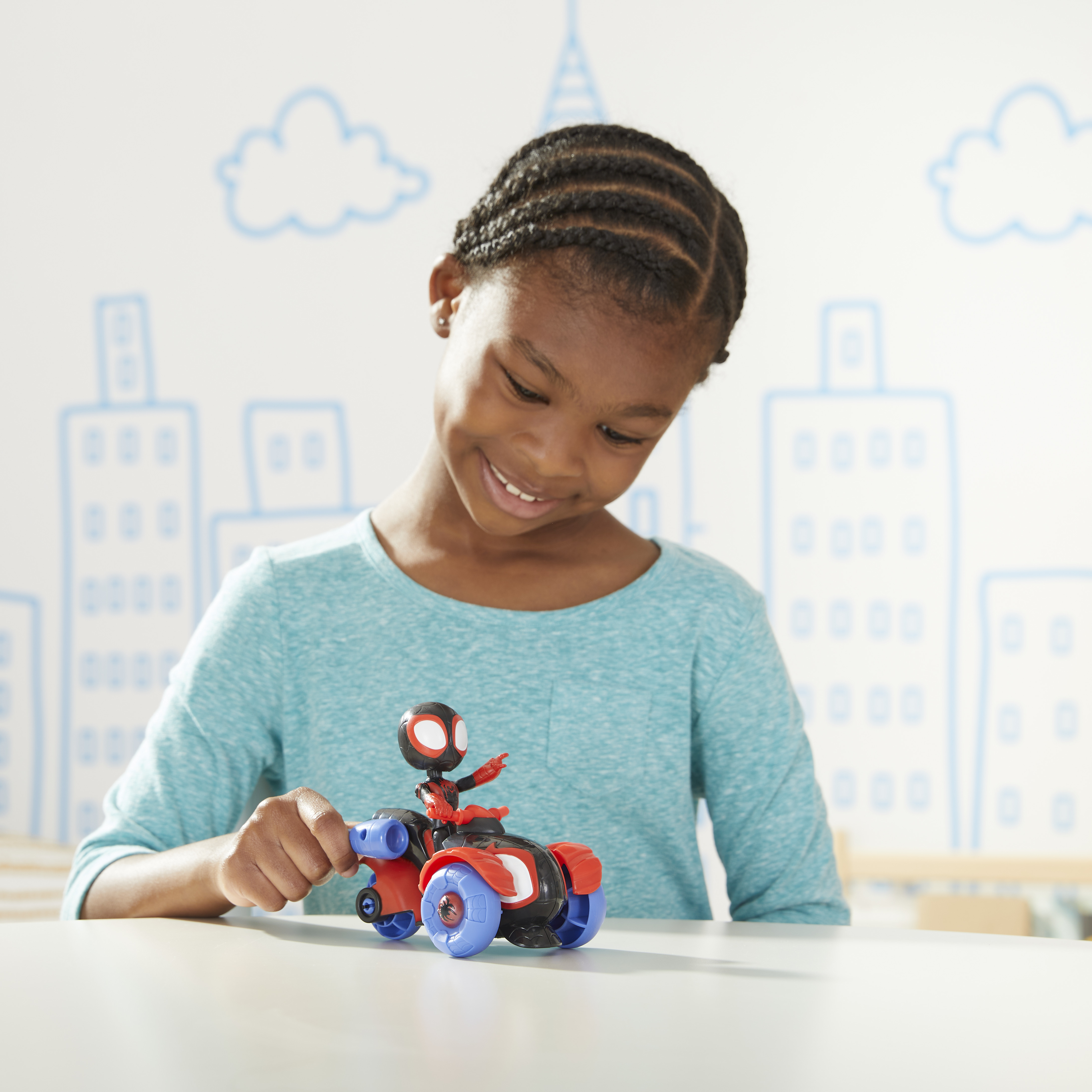 Una ragazza sorride mentre tiene in mano un giocattolo di Miles Morales Spider-Man. Davanti c'è una moto blu e rossa.