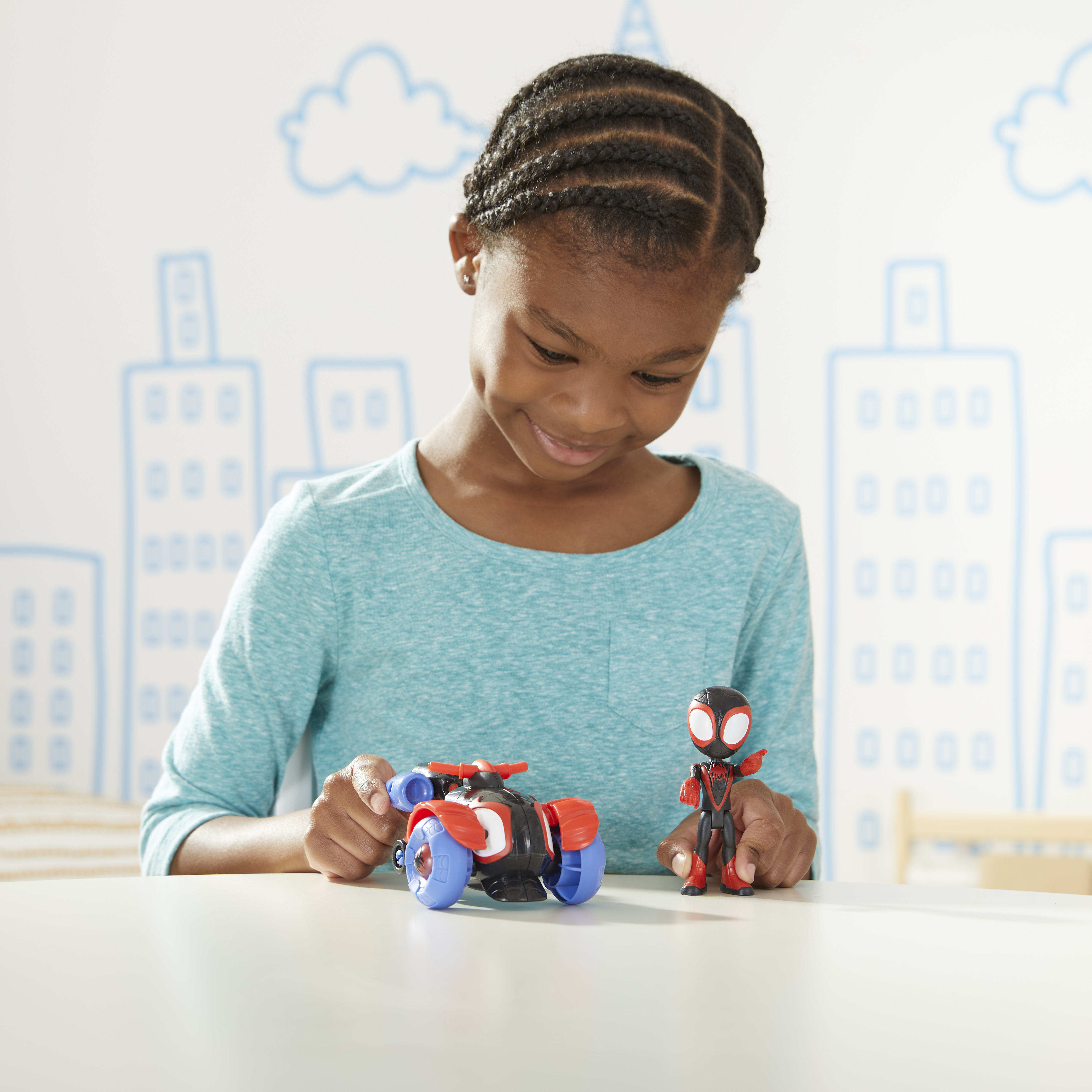 Una ragazzina gioca con una moto giocattolo e un'action figure di Miles Morales su un tavolo.