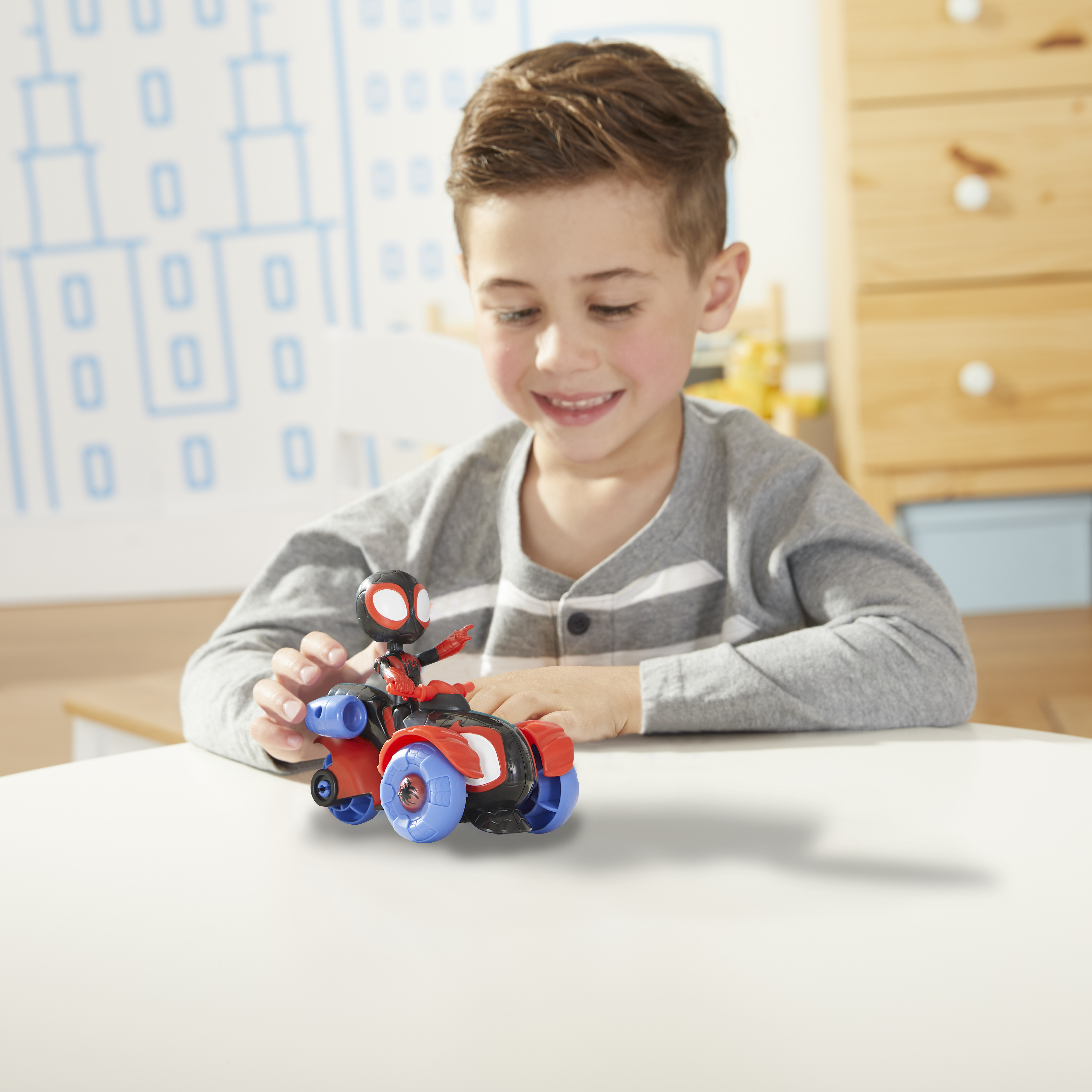 Un ragazzo sorride mentre tiene in mano un giocattolo di Miles Morales Spider-Man. Davanti c'è una moto blu e rossa.