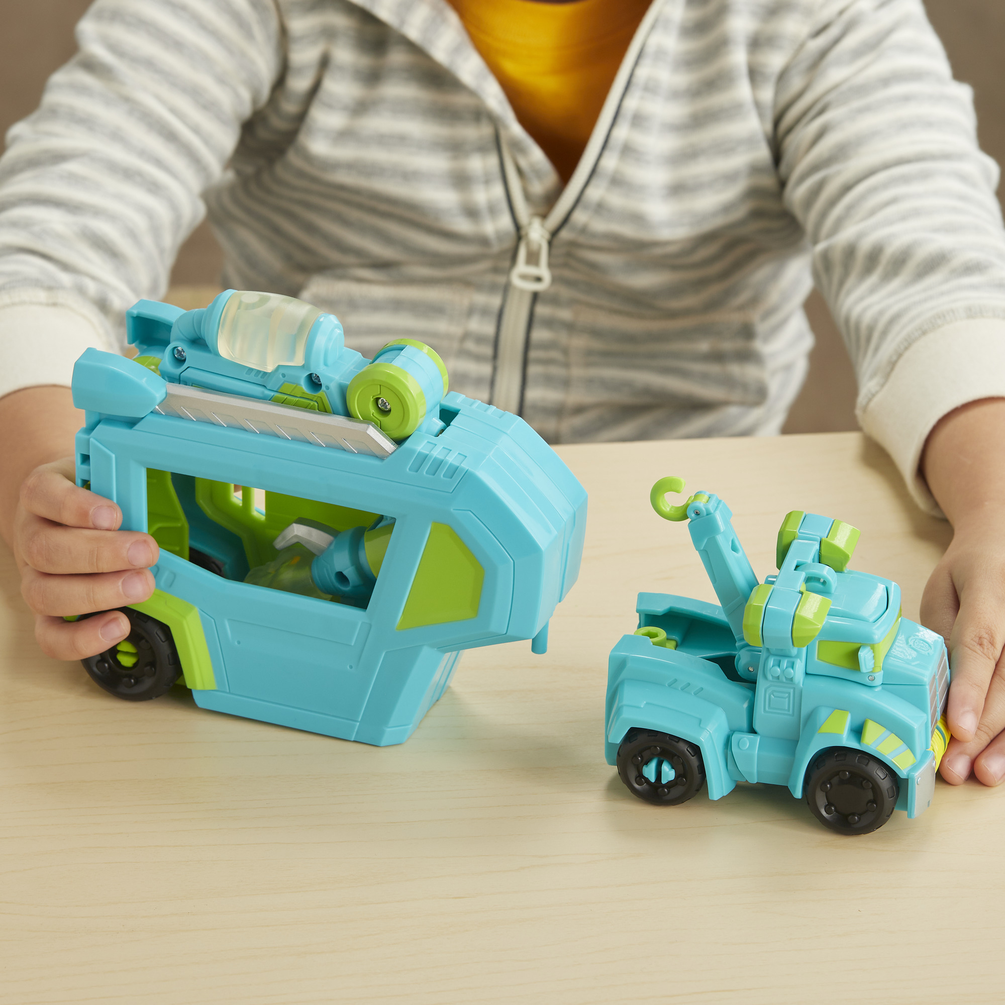Un bambino gioca con un camion e un rimorchio giocattolo blu e verde su un tavolo di legno.