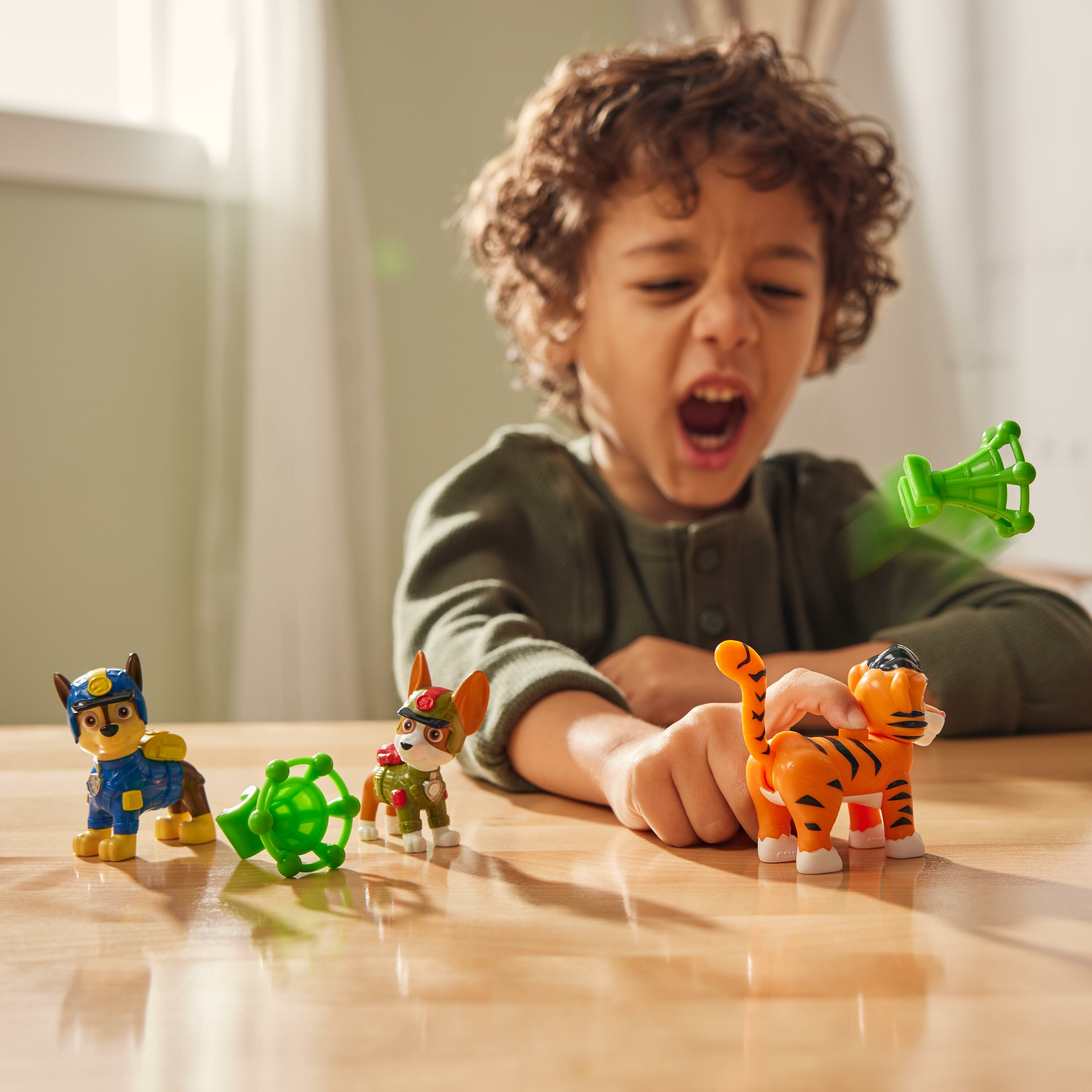 Kind betrachtet Paw Patrol Figuren, grüne Werfer und Tigerspielzeug.