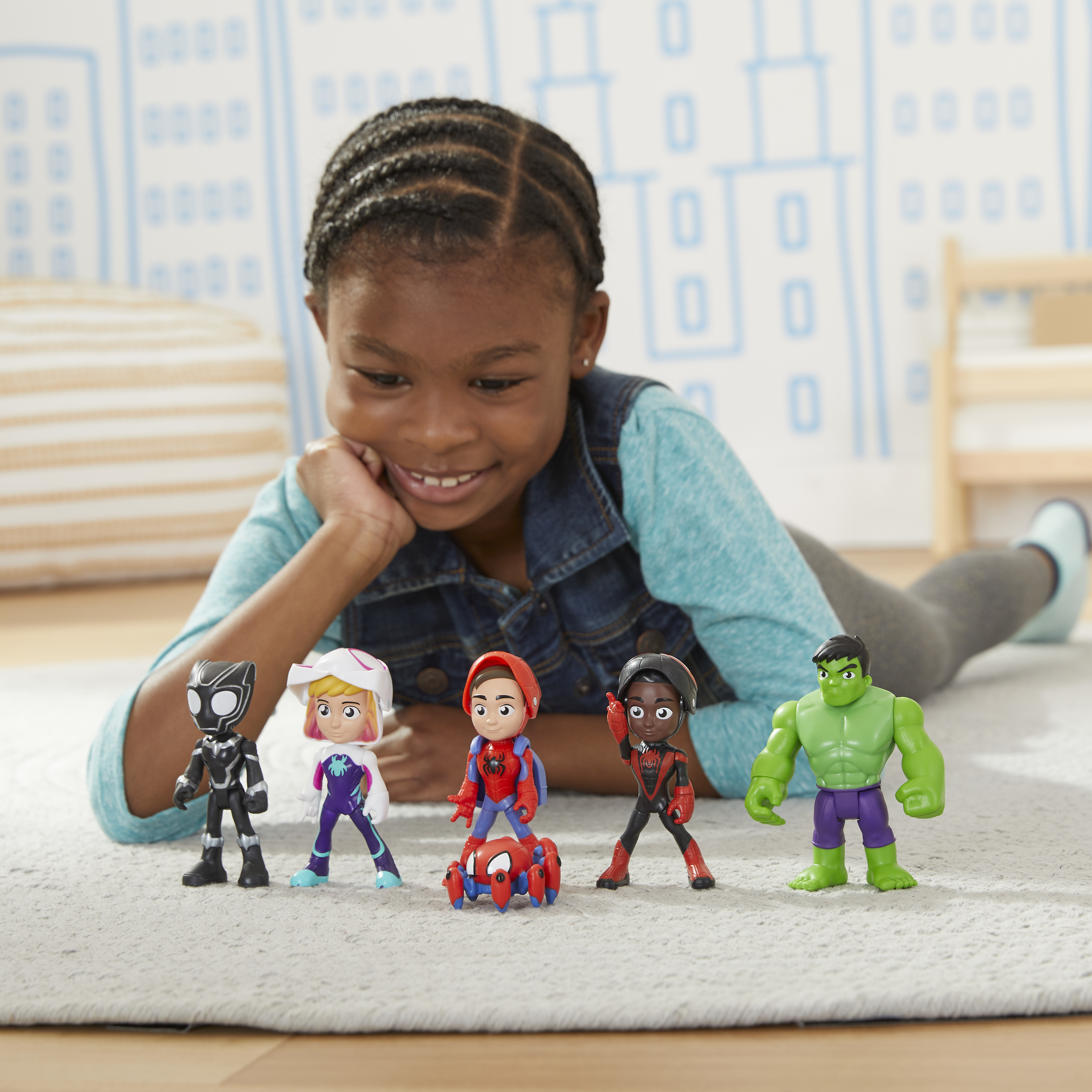 Bambina con giocattoli Marvel. Include Spider-Man, Hulk e altri personaggi. Sdraiata sul pavimento.