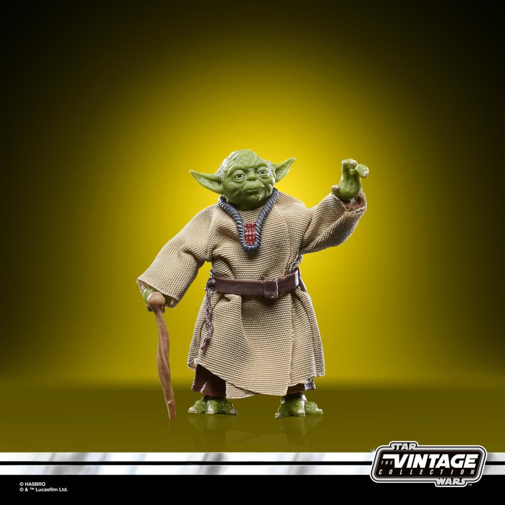 Yoda figürü, yeşil ten, kahverengi cübbe, baston tutuyor, sarı bir arka plan üzerinde duruyor.
