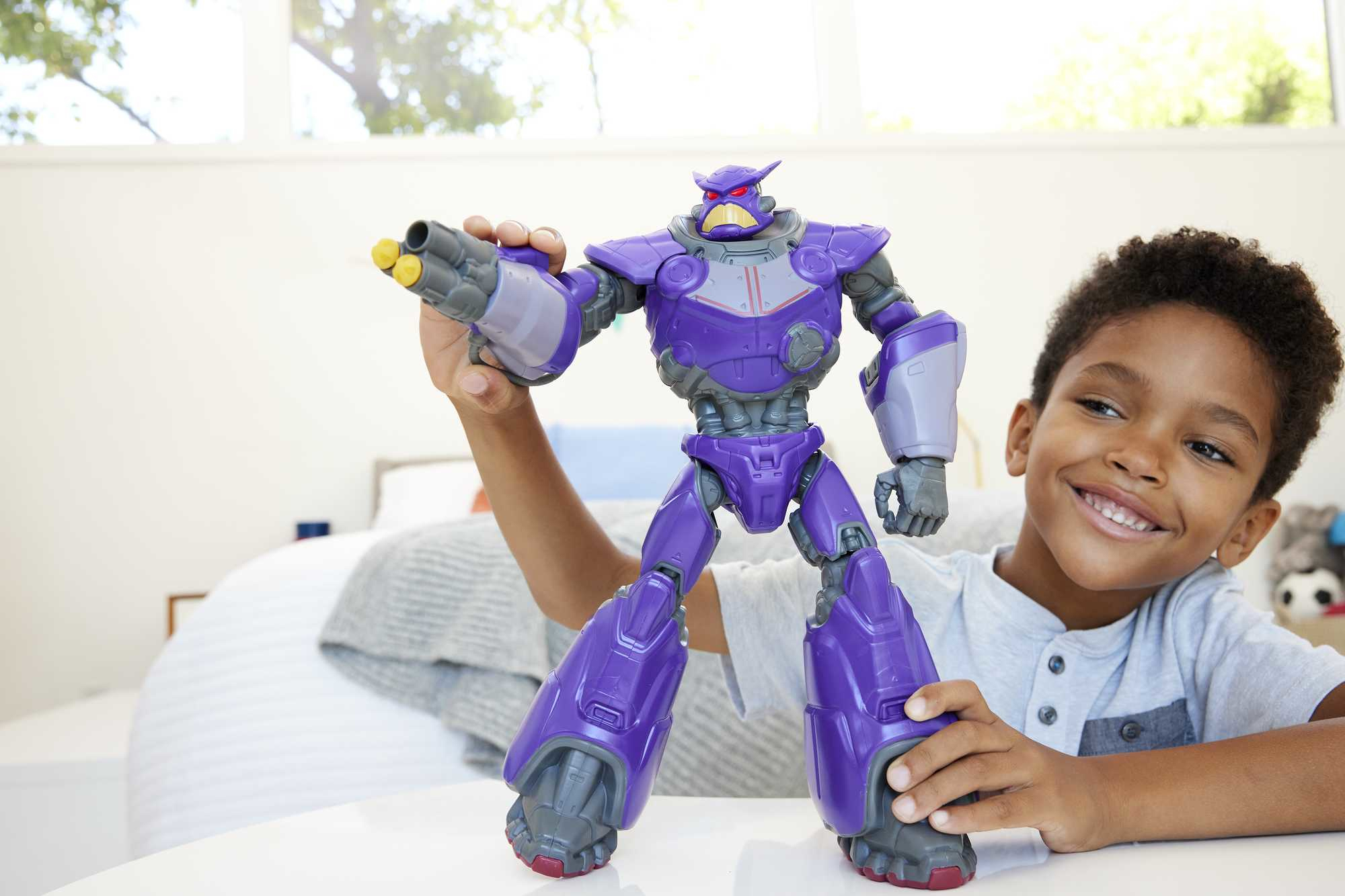 Un bambino che tiene un giocattolo robot viola. Il giocattolo ha una pistola grande e il bambino sorride.