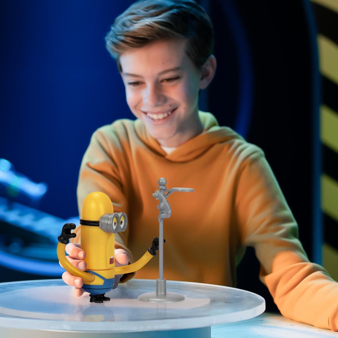 Un ragazzo sorride mentre gioca con un giocattolo Minion. Il Minion tiene un rubinetto d'argento su una piattaforma rotante.