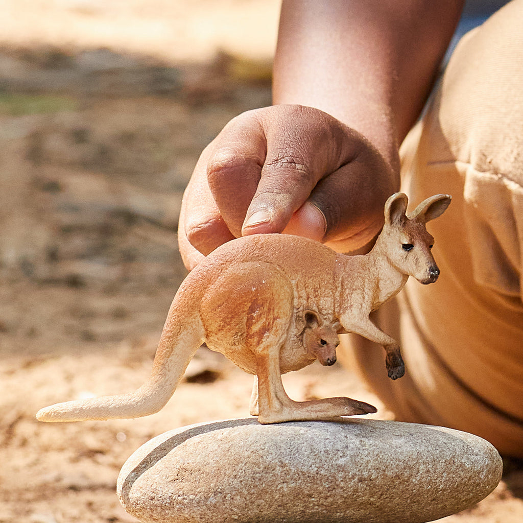 Un canguro giocattolo con un bambino nella sua tasca. La mano di una persona tiene il giocattolo. Sfondo beige.