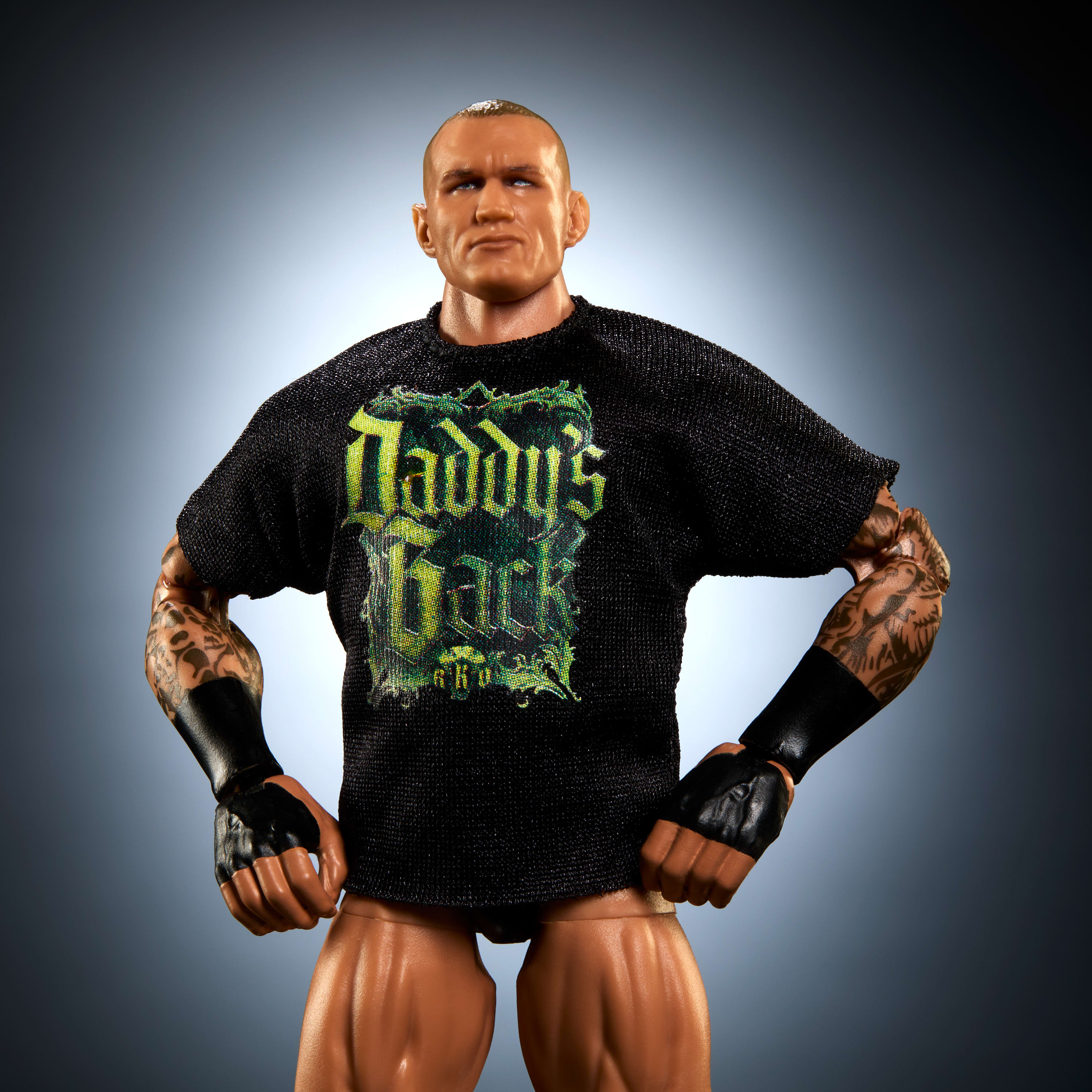 Actionfigur eines Mannes mit Tätowierungen, in einem schwarzen Hemd mit grüner Schrift. Er steht mit den Händen in den Hüften.