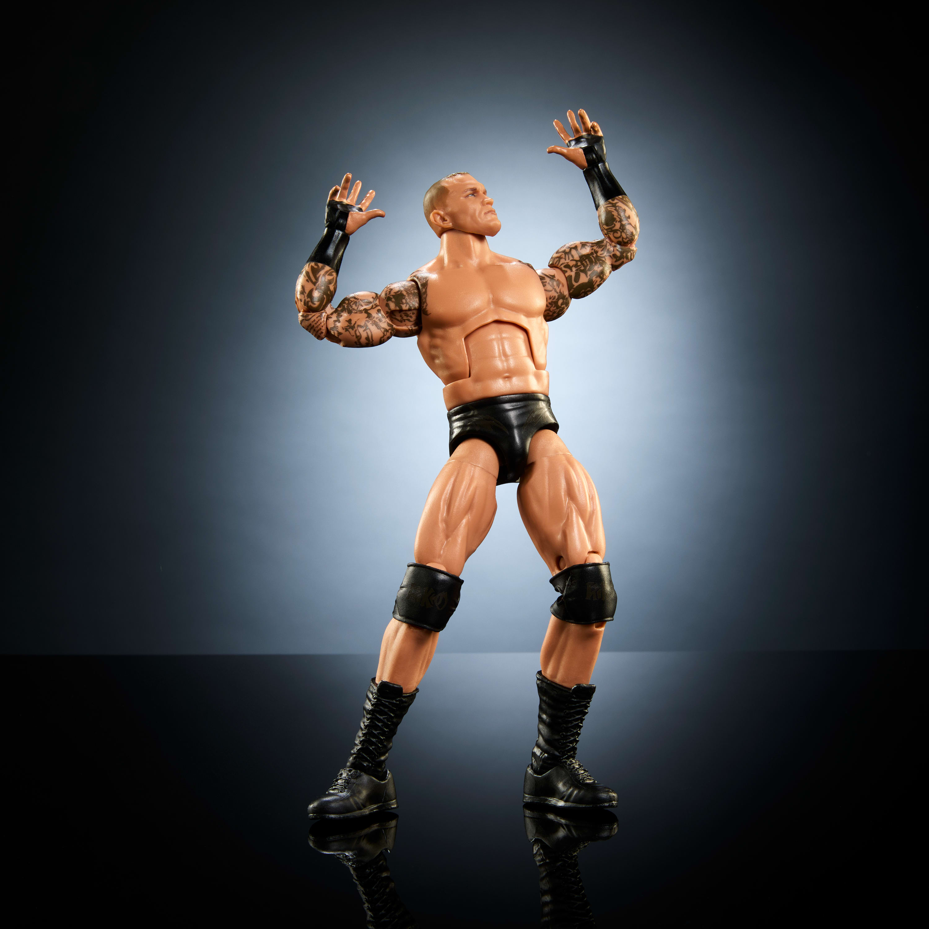 Actionfigur eines muskulösen Wrestlers mit Tattoos, Arme erhoben. Schwarze Shorts und Knieschützer.