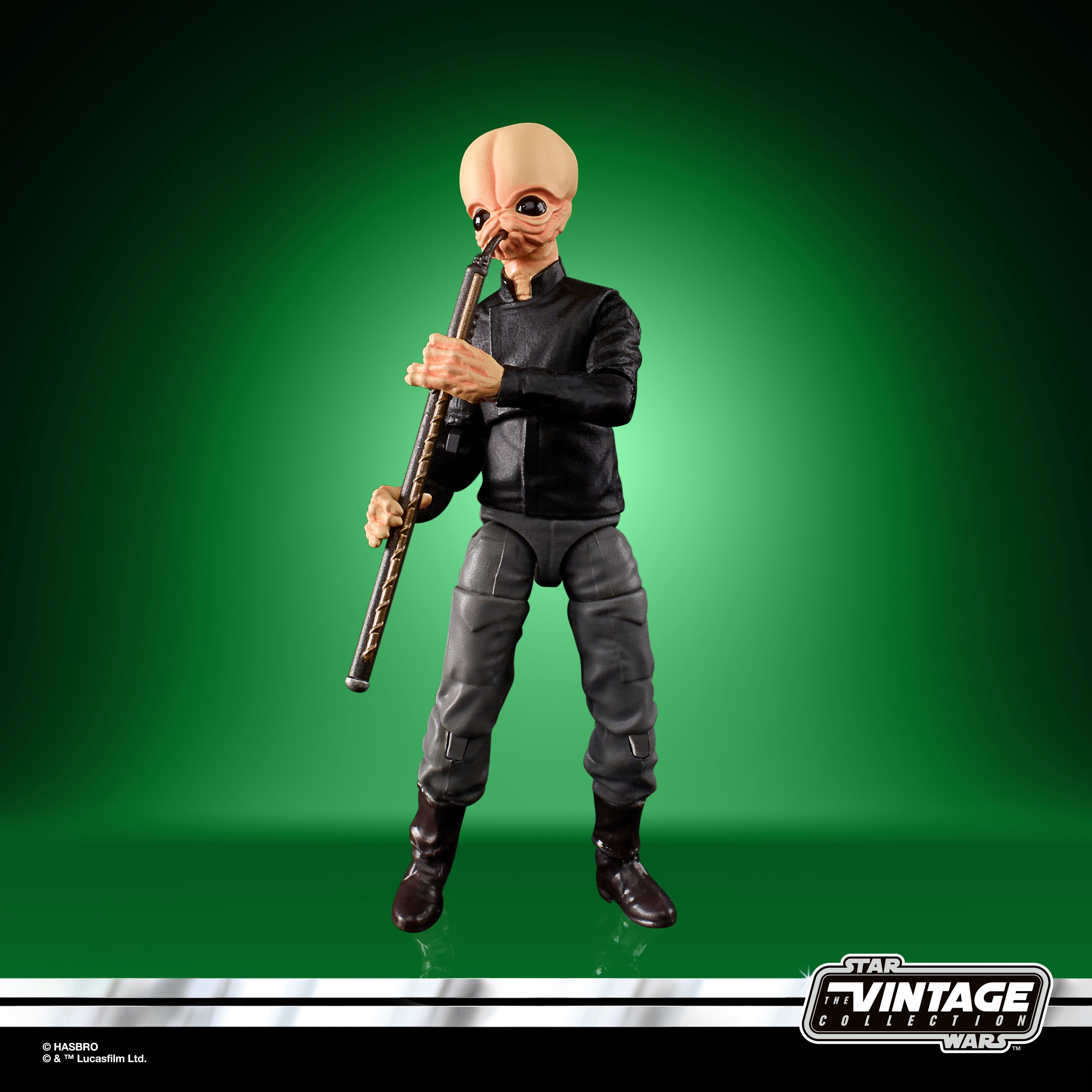 Eine Spielfigur eines glatzköpfigen Aliens, der vor grünem Hintergrund Flöte spielt.