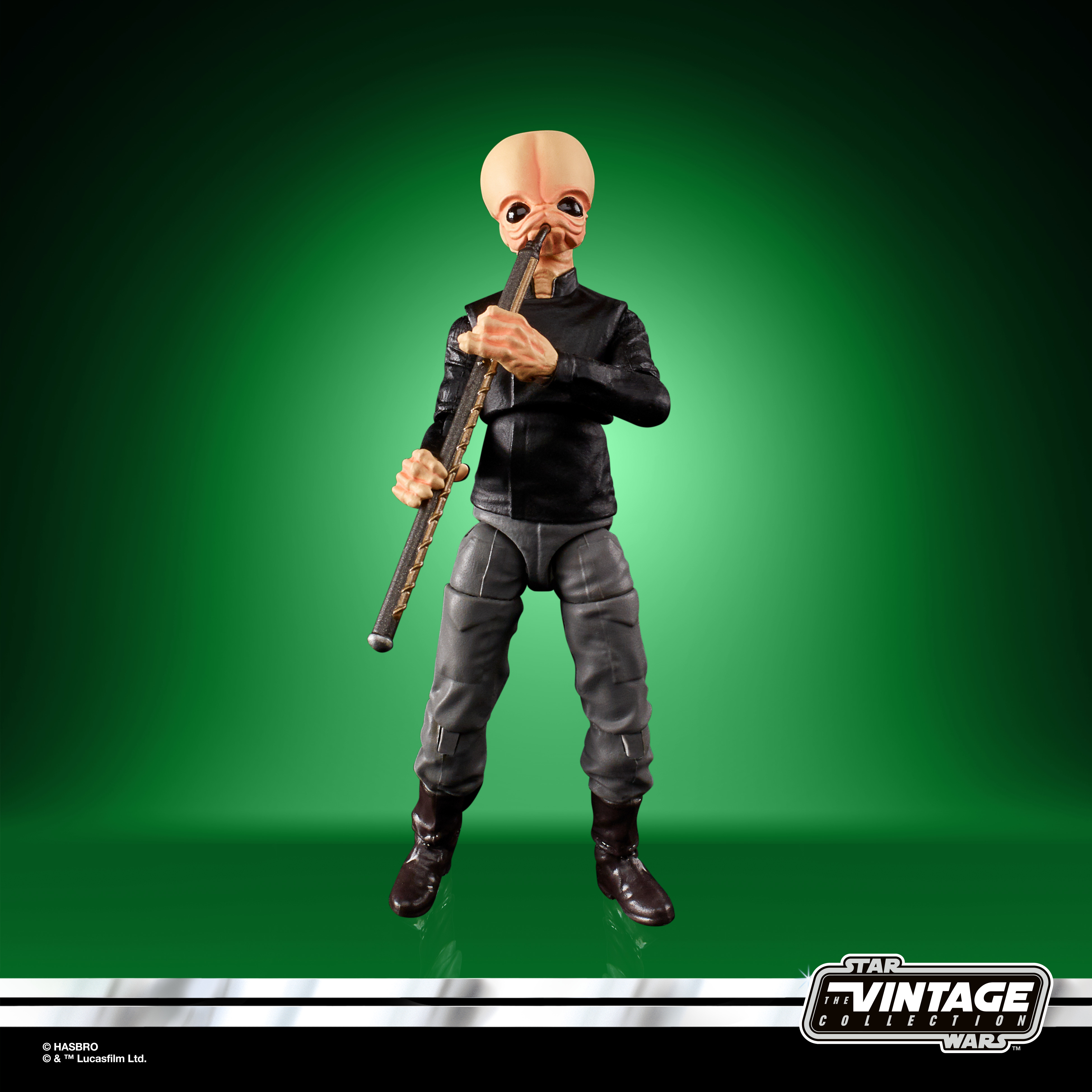 Eine Spielzeugfigur eines Aliens, das vor grünem Hintergrund Flöte spielt.