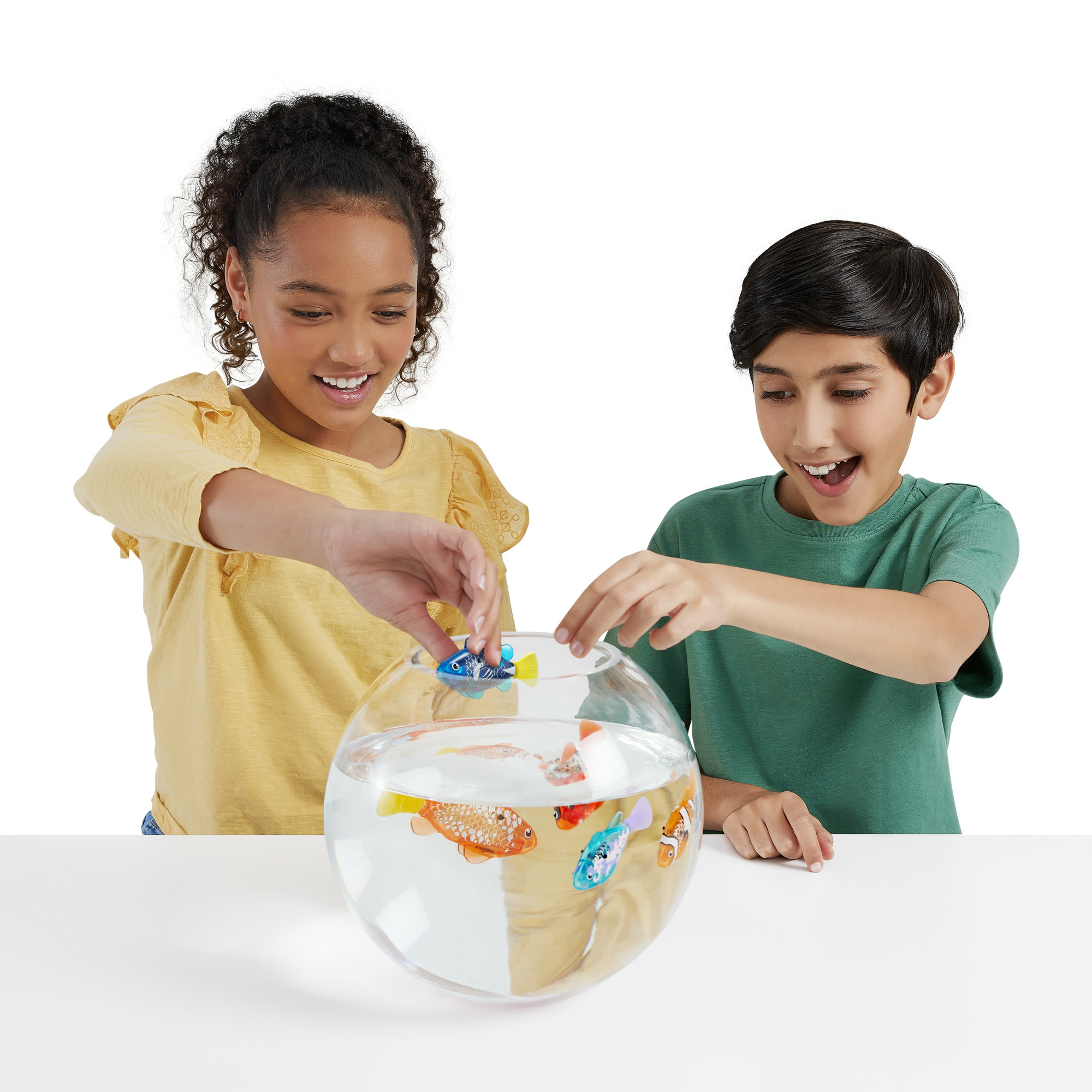 Due bambini che giocano con pesci giocattolo in una ciotola di vetro piena d'acqua. Sfondo bianco.