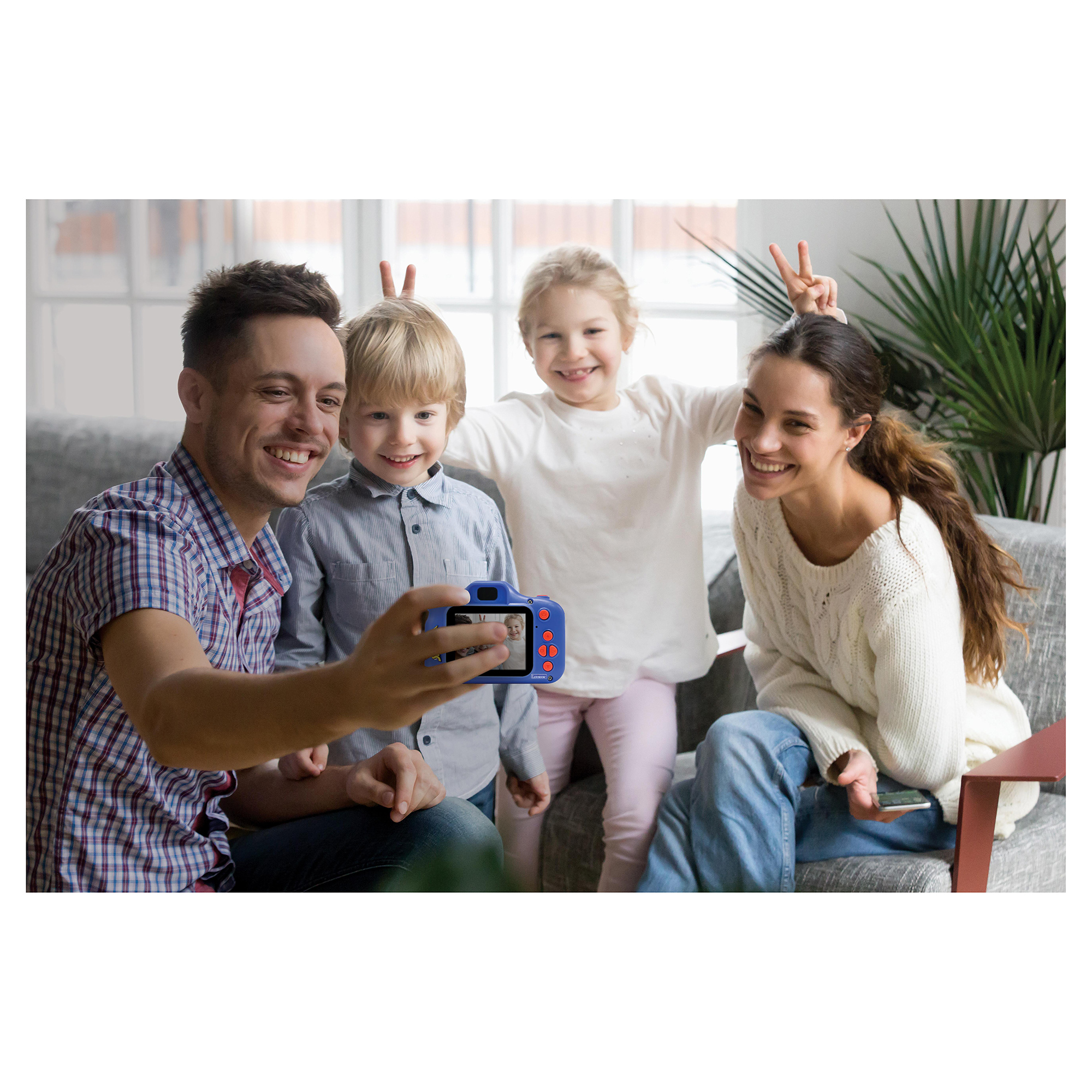 Rodzina robi selfie z niebieskim aparatem. Uśmiechy i znaki pokoju. Wnętrze z szarą sofą.